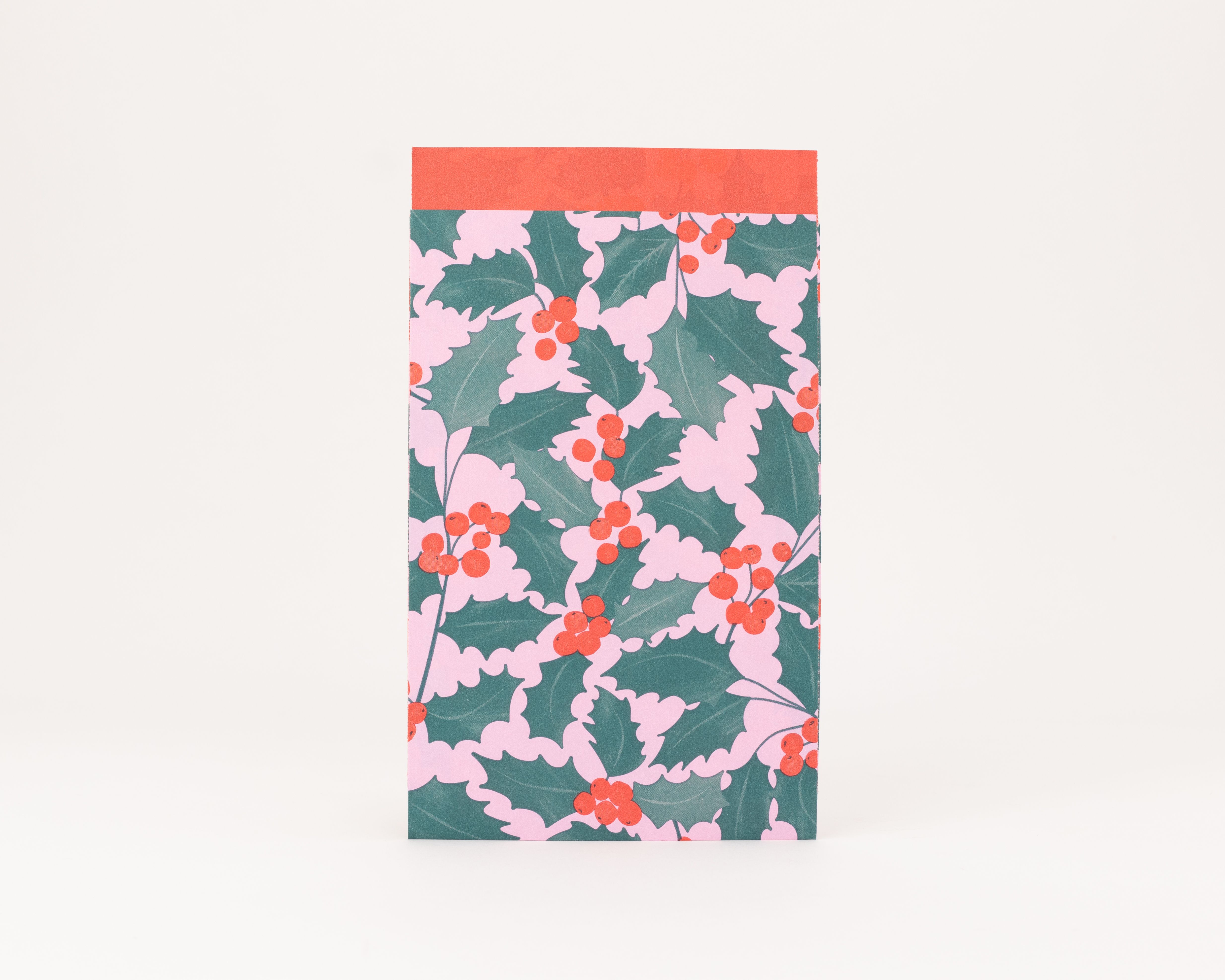Flachbeutel mit einem Ilex-Muster aus grünen Blättern und roten Beeren auf rosa Hintergrund, die Innenseite ist einfarbig rot