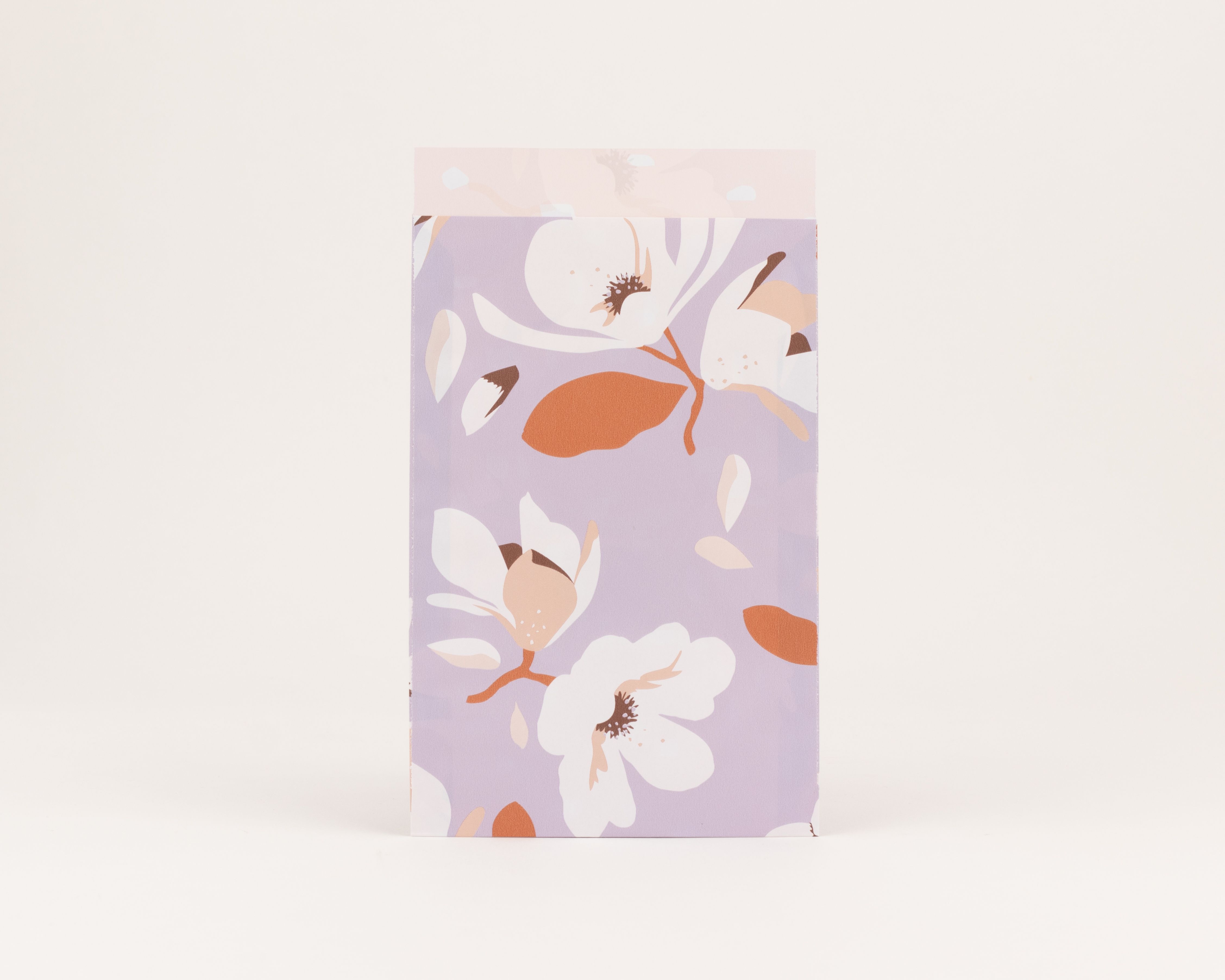 Flachbeutel mit einem blumigen Magnolienmuster in Flieder, Weiß, Braun und Rostfarben. Die Innenseite ist in Beige gehalten