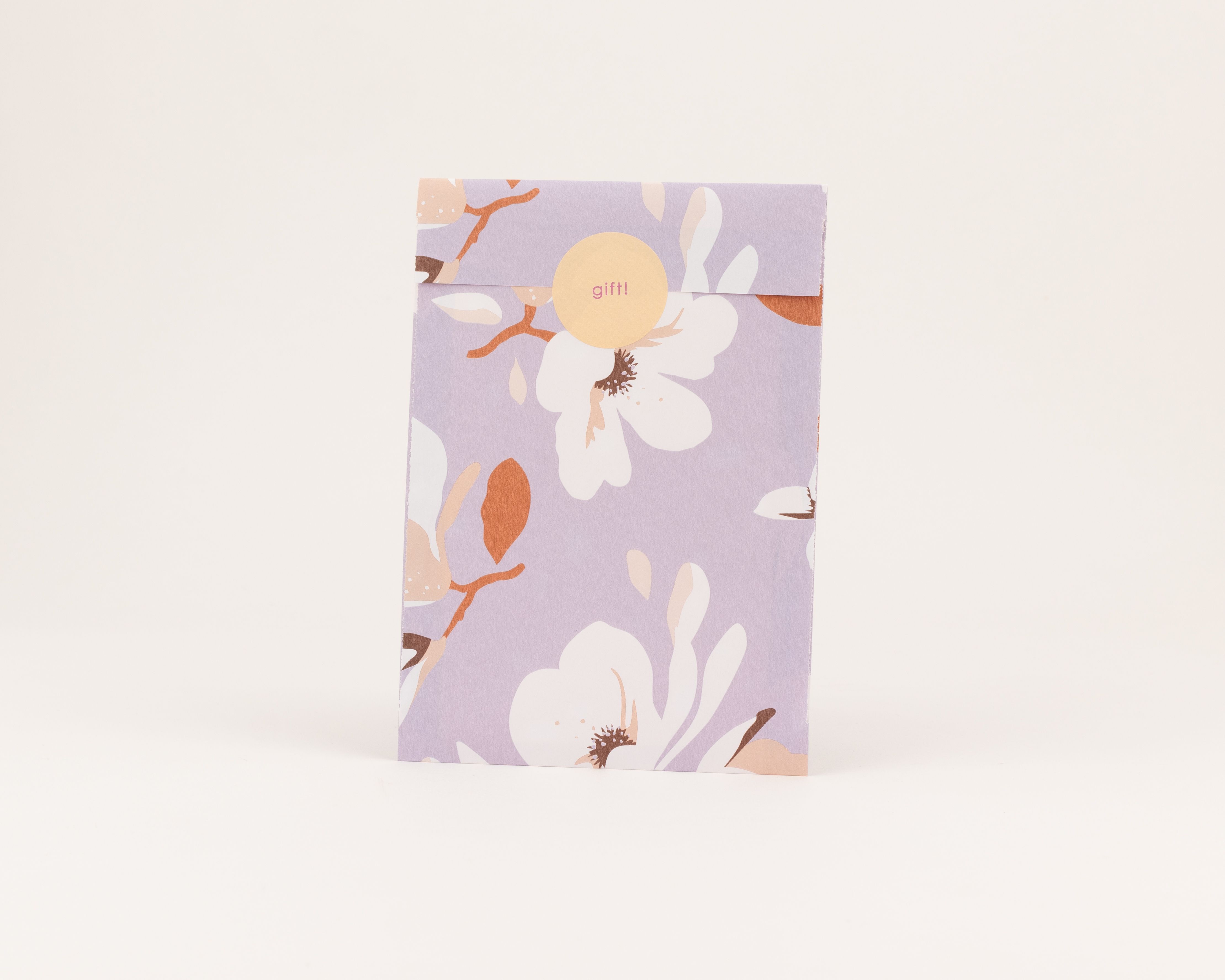 Flachbeutel mit Magnolien und Zweigen in Weiß, Braun, Rost und Beige auf fliederfarbenem Papier Die Innenseite hat dasselbe florale Muster