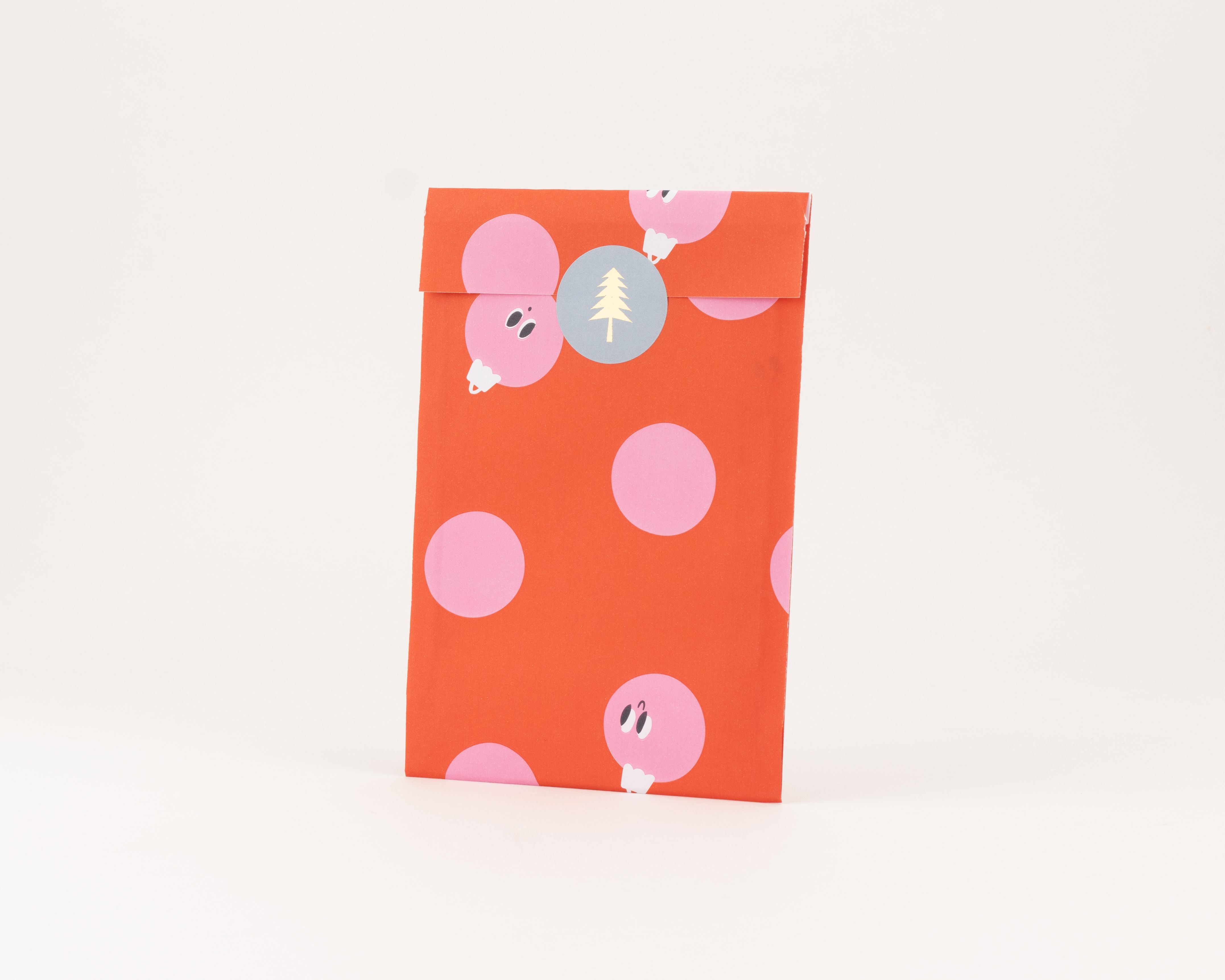 Flachbeutel in Rot mit pinken Punkten und verspielten Bauble-Motiven, verziert mit einem Sticker mit gelbem Weihnachtsbaum