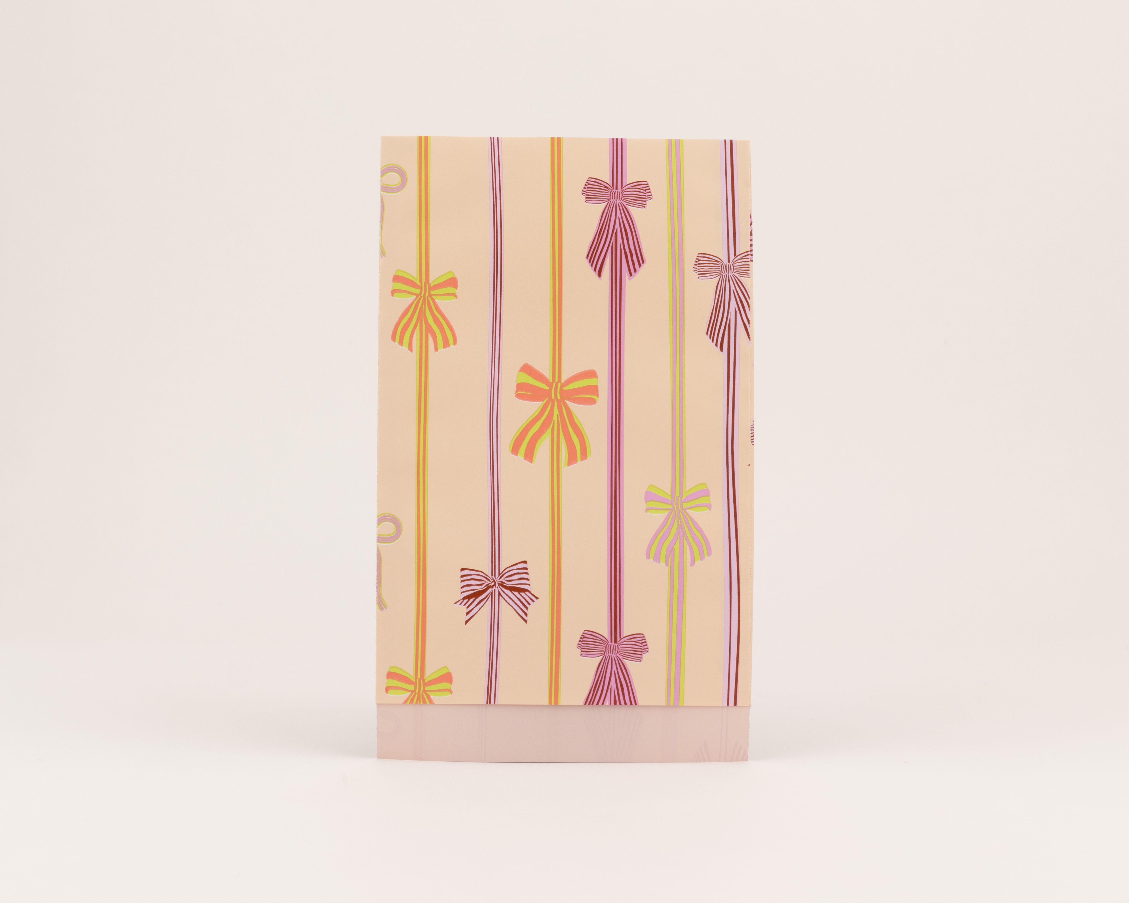 Flachbeutel mit Schleifen und Streifen in Pink, Grün, Hellviolett, Limettengrün auf Aprikot. Die Innenseite ist Pink