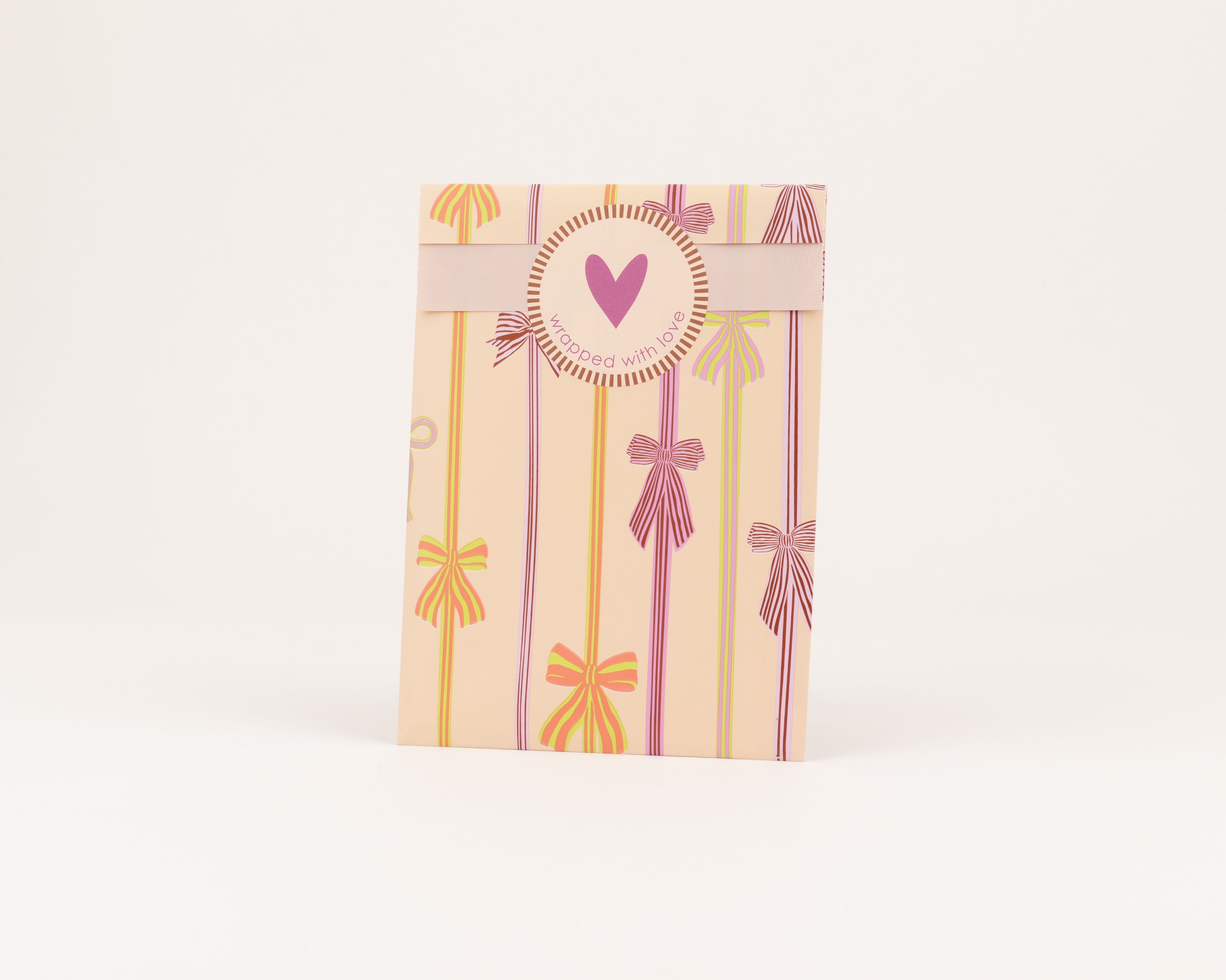 Flachbeutel mit aprikotfarbenem Grundton und Schleifenmuster in Pink, Grün, Hellviolett und Limettengrün. Die Innenseite ist einfarbig hellrosa