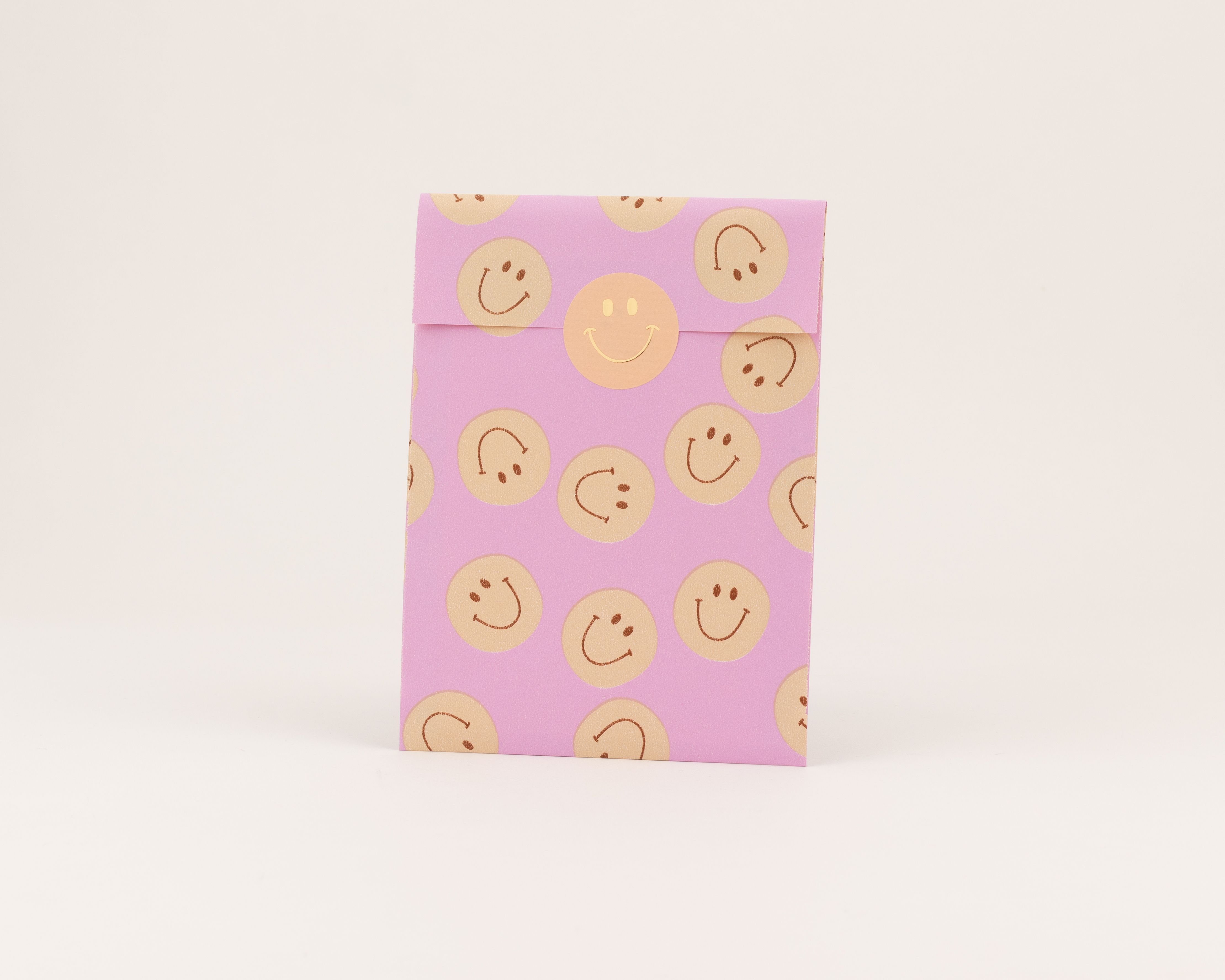 Flachbeutel in Fliederfarbe mit einem Muster aus beigen Smileys und orangen Konturen. Die Innenseite ist fliederfarben mit beigen Smileys