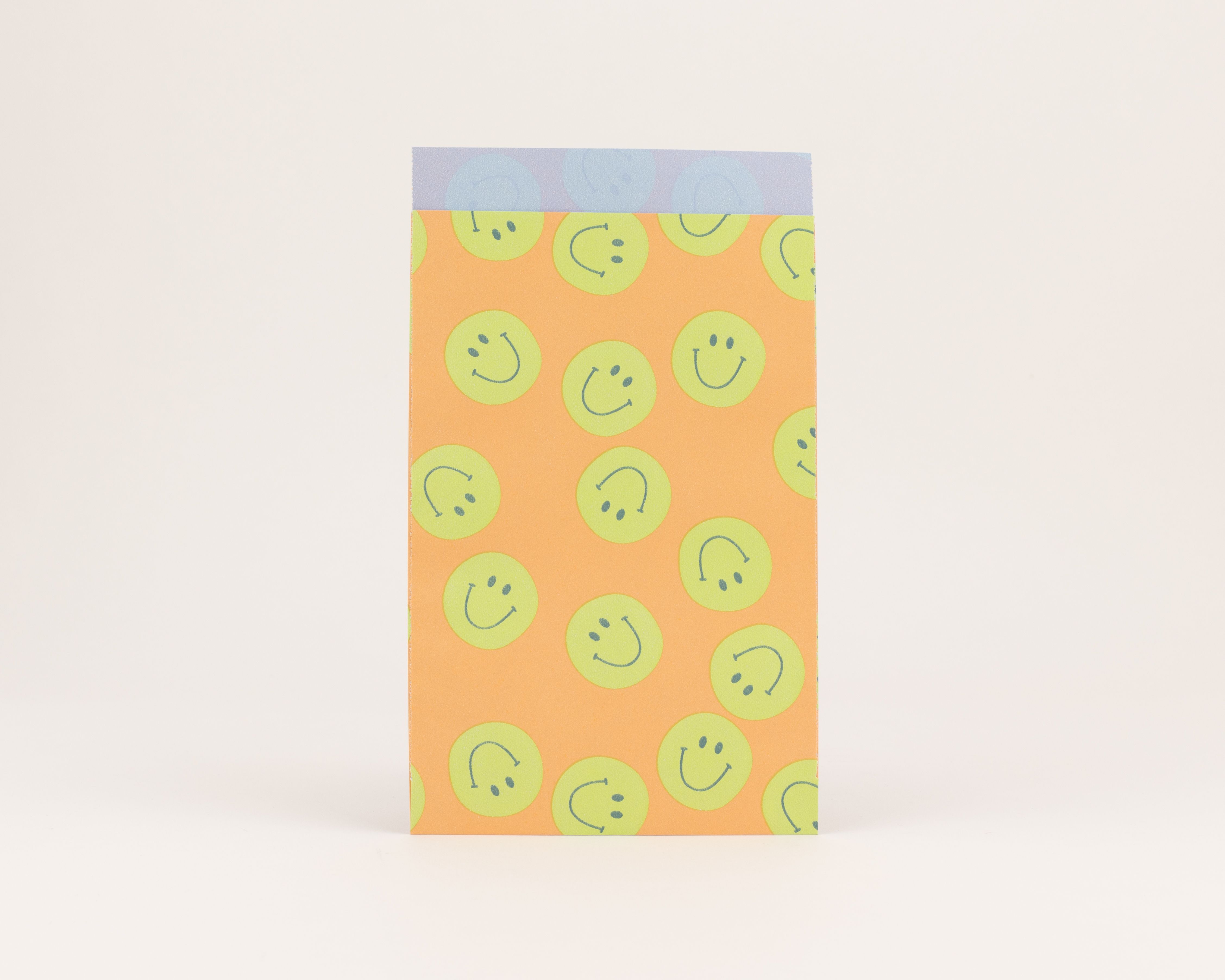 Flachbeutel mit einem auffälligen Smiley-Muster in Orange und Grün, die Innenseite ist Blau mit dezenten Kreismotiven