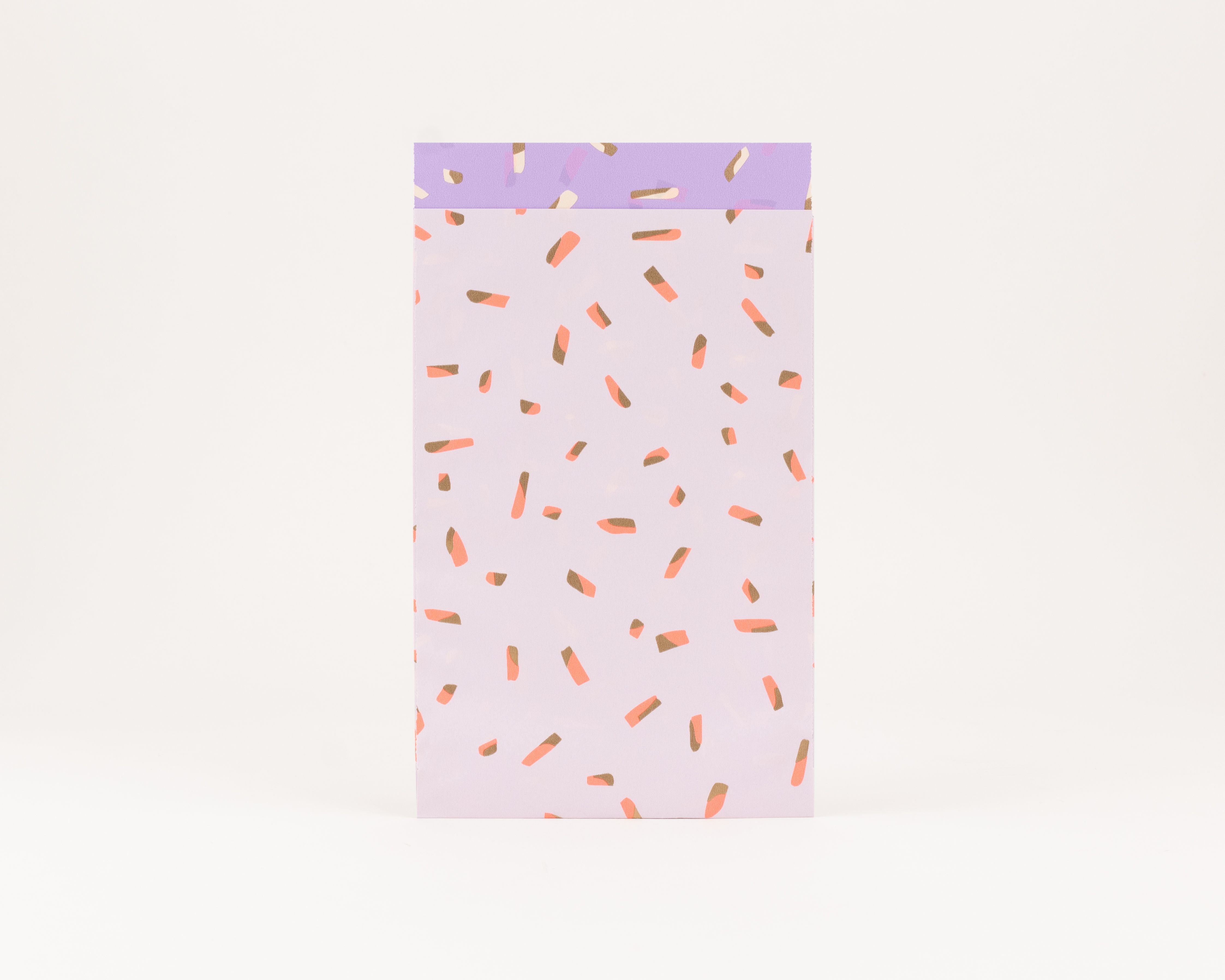 Flachbeutel in hellem Flieder mit Koralle- und Goldeffekt-Sprinkles. Die Innenseite zeigt das gleiche Muster in Violett, Elfenbein und Gold.