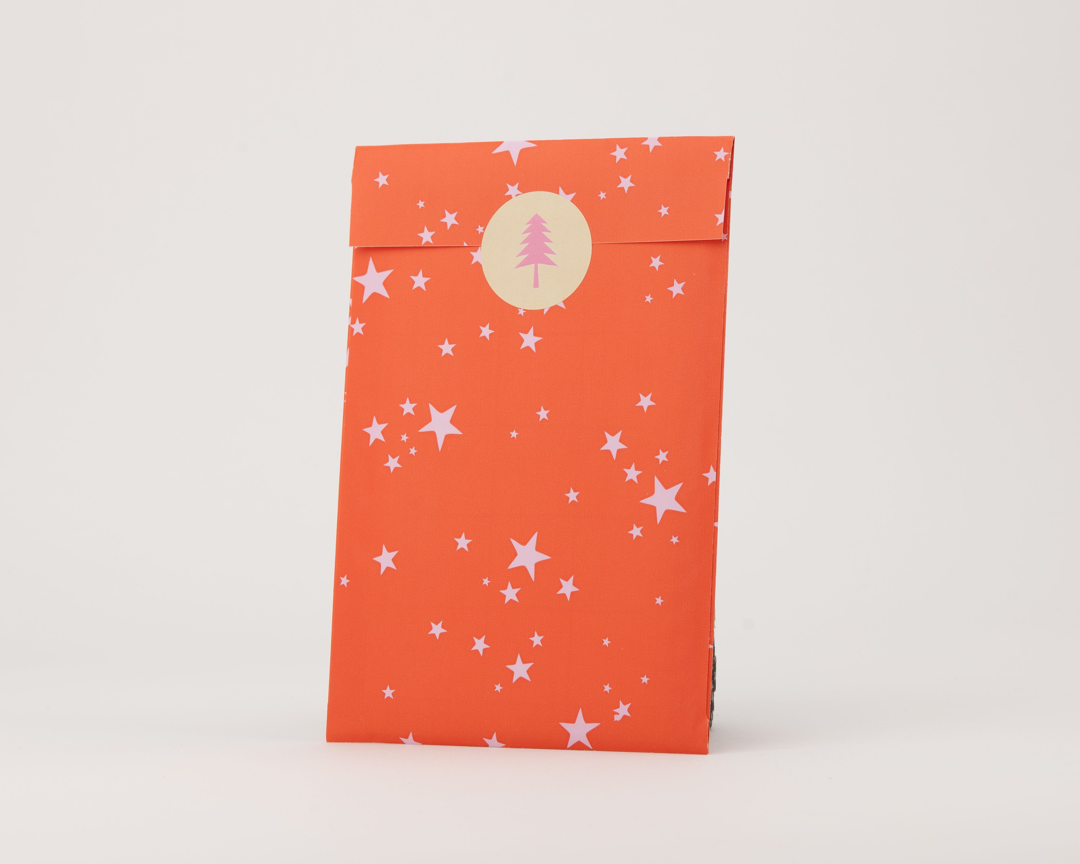 Papiertüten Flachbeutel in Orangerot mit rosafarbenen Sternen und einer hellrosa Innenseite, verziert mit Tannenbaum-Aufkleber.