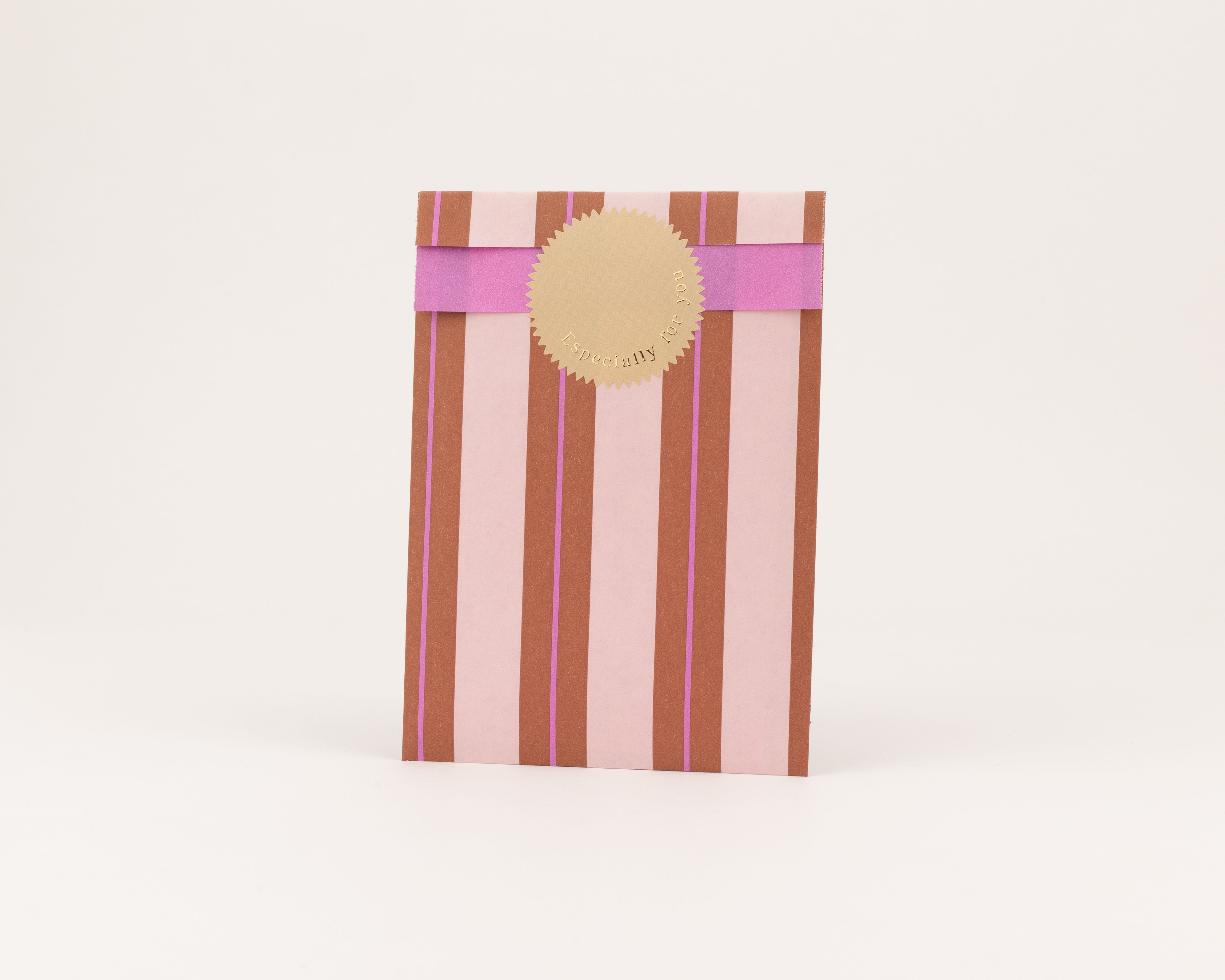 Flachbeutel mit vertikalen Streifen in Hellrosa und Braun auf der Außenseite, ergänzt durch feine Lila Linien. Die Innenseite zeigt sich in einem kräftigen Pink.