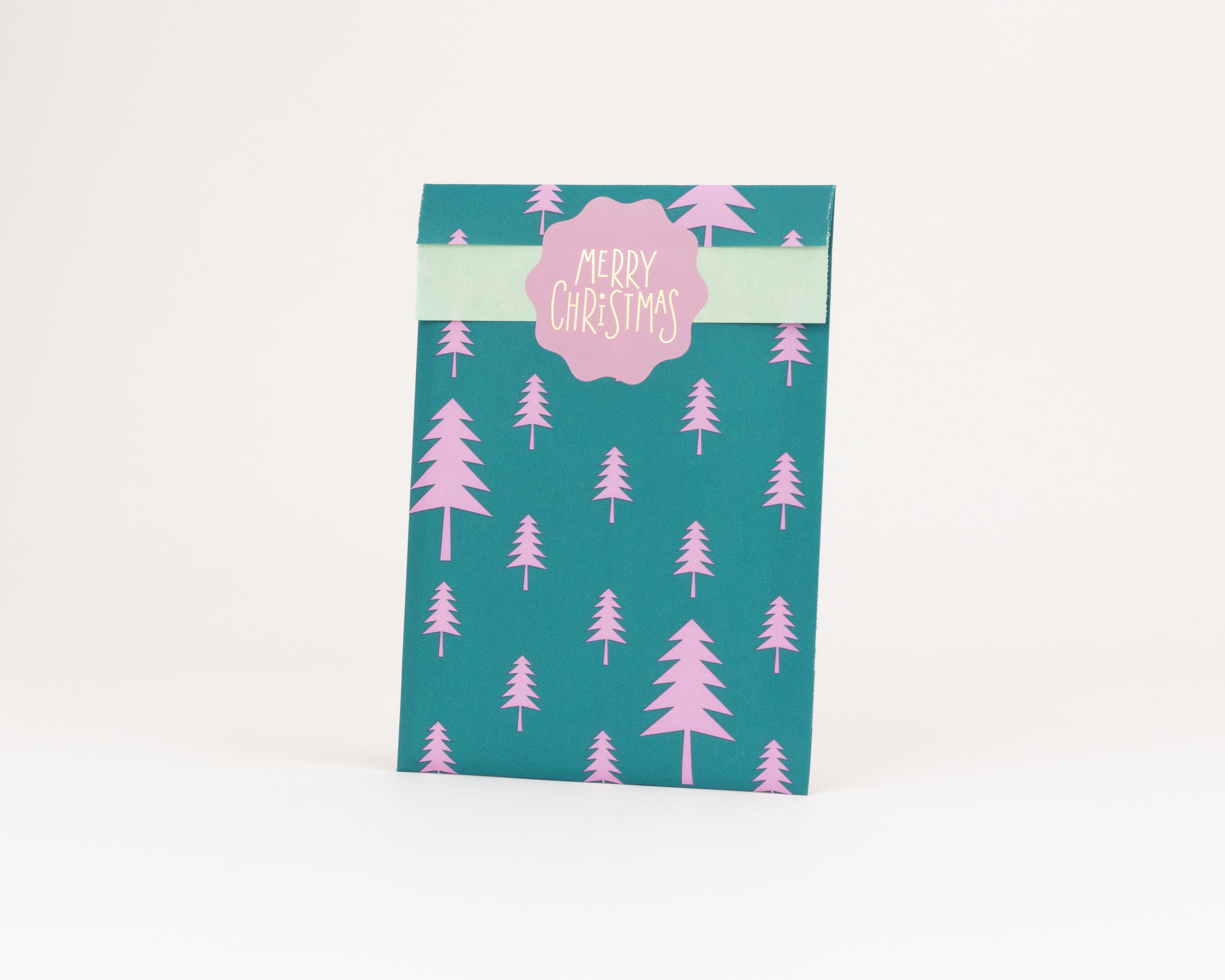 Flachbeutel mit grünem Außenmuster, bestehend aus pinken Tannenbäumen, und einer hellgrünen Innenseite mit einem 'Merry Christmas' Schriftzug
