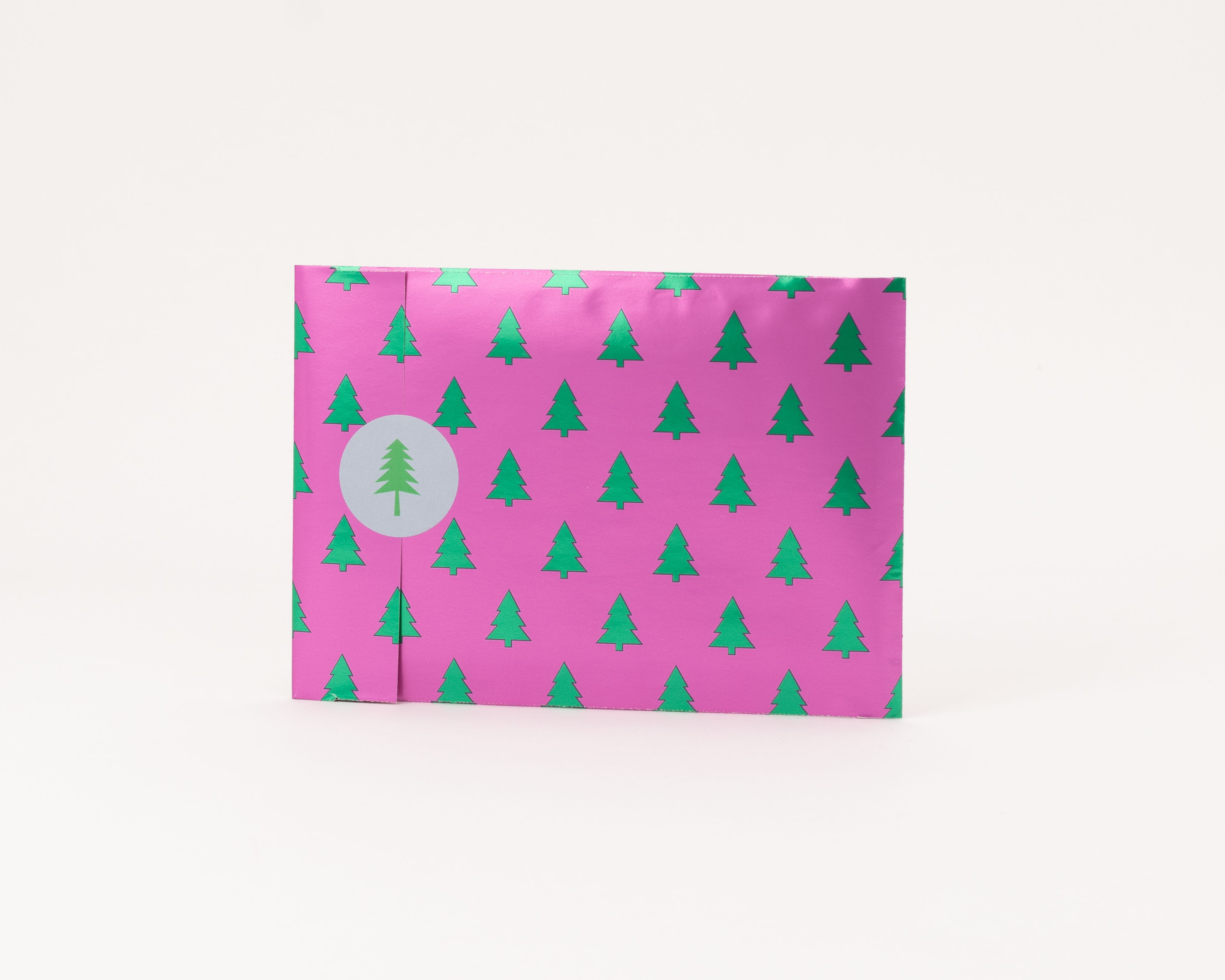Flachbeutel in Pink mit wiederholendem Muster aus grünen, metallisch schimmernden Tannen, die Innenseite ist beige