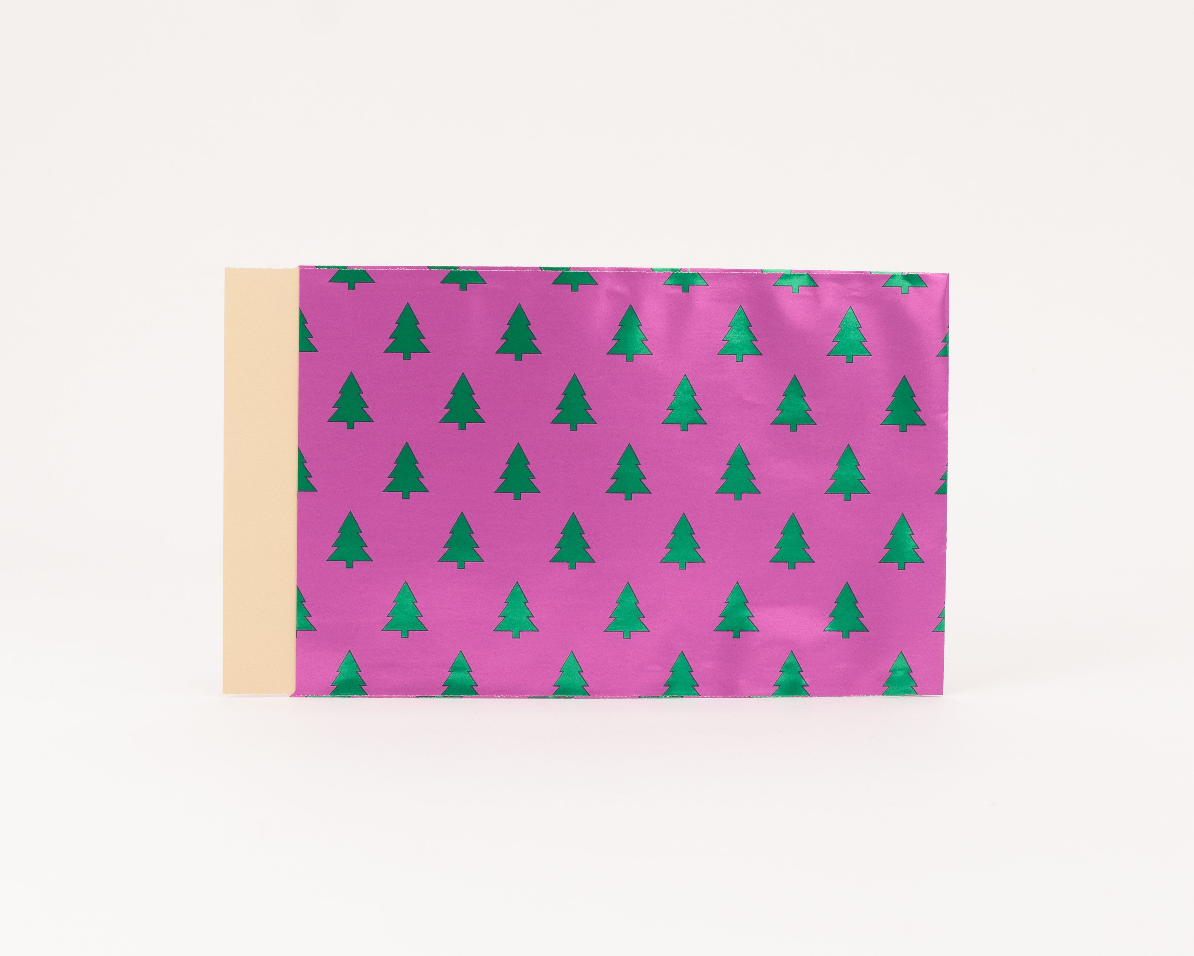 Flachbeutel mit pinker Außenseite und einem Muster aus metallisch grünen Tannenbäumen, die Innenseite ist beige