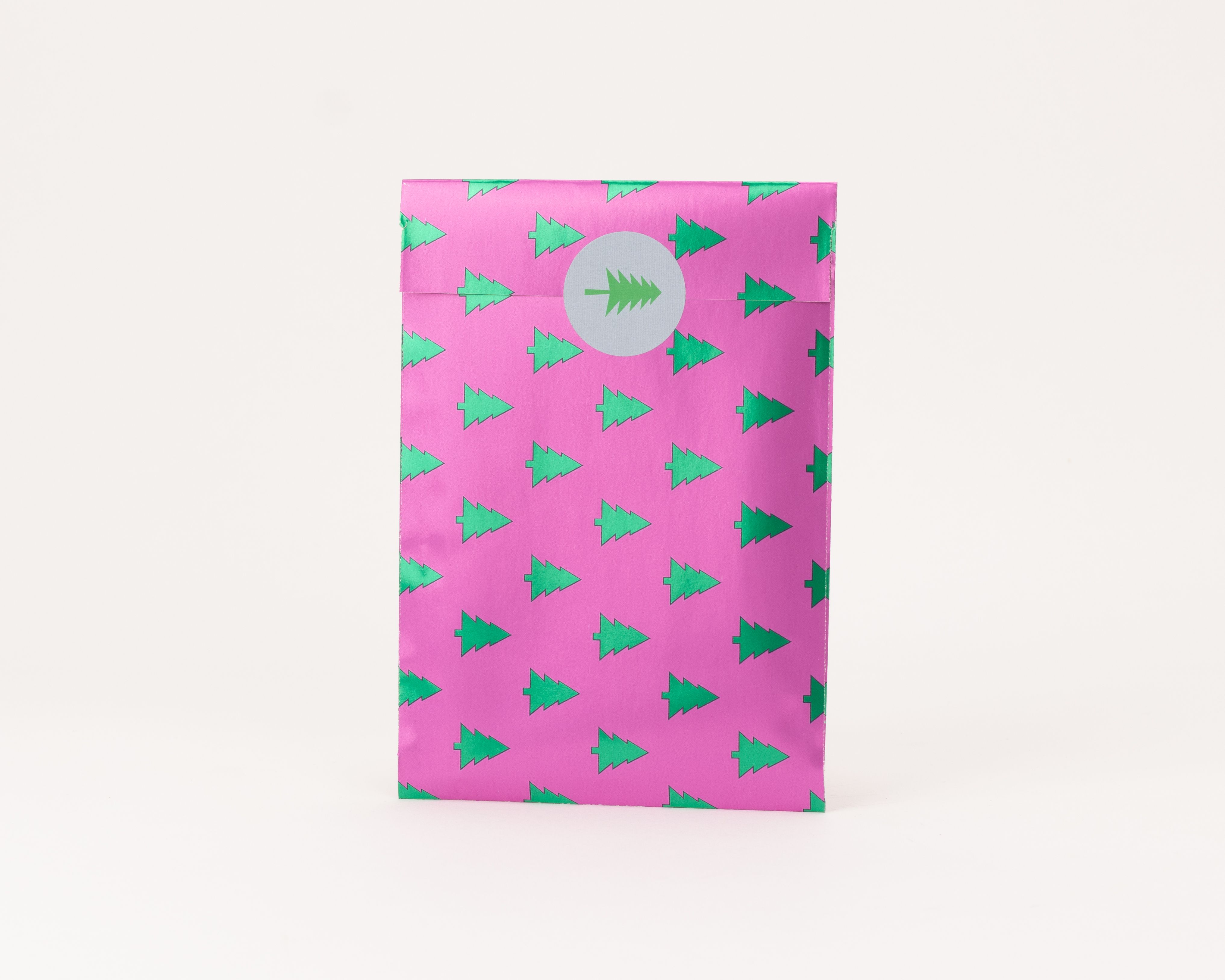 Flachbeutel in leuchtendem Pink, bedruckt mit einem Muster aus grünen, metallisch glänzenden Tannenbäumen