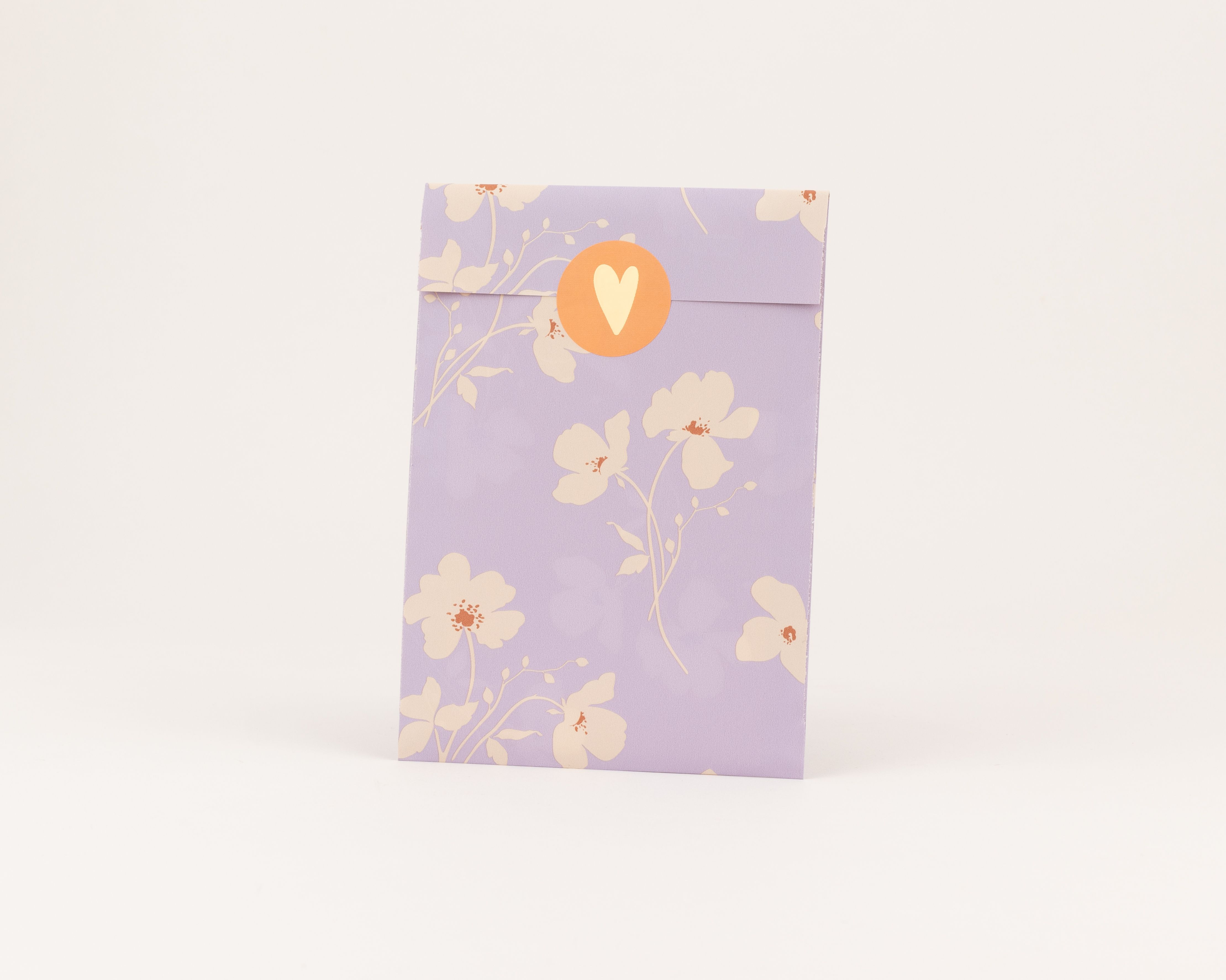 Flachbeutel in Flieder mit beigem Wiesenblütenmuster und rostenfarbenen Details, ergänzt durch einen rostfarbenen Aufkleber mit beigem Herz