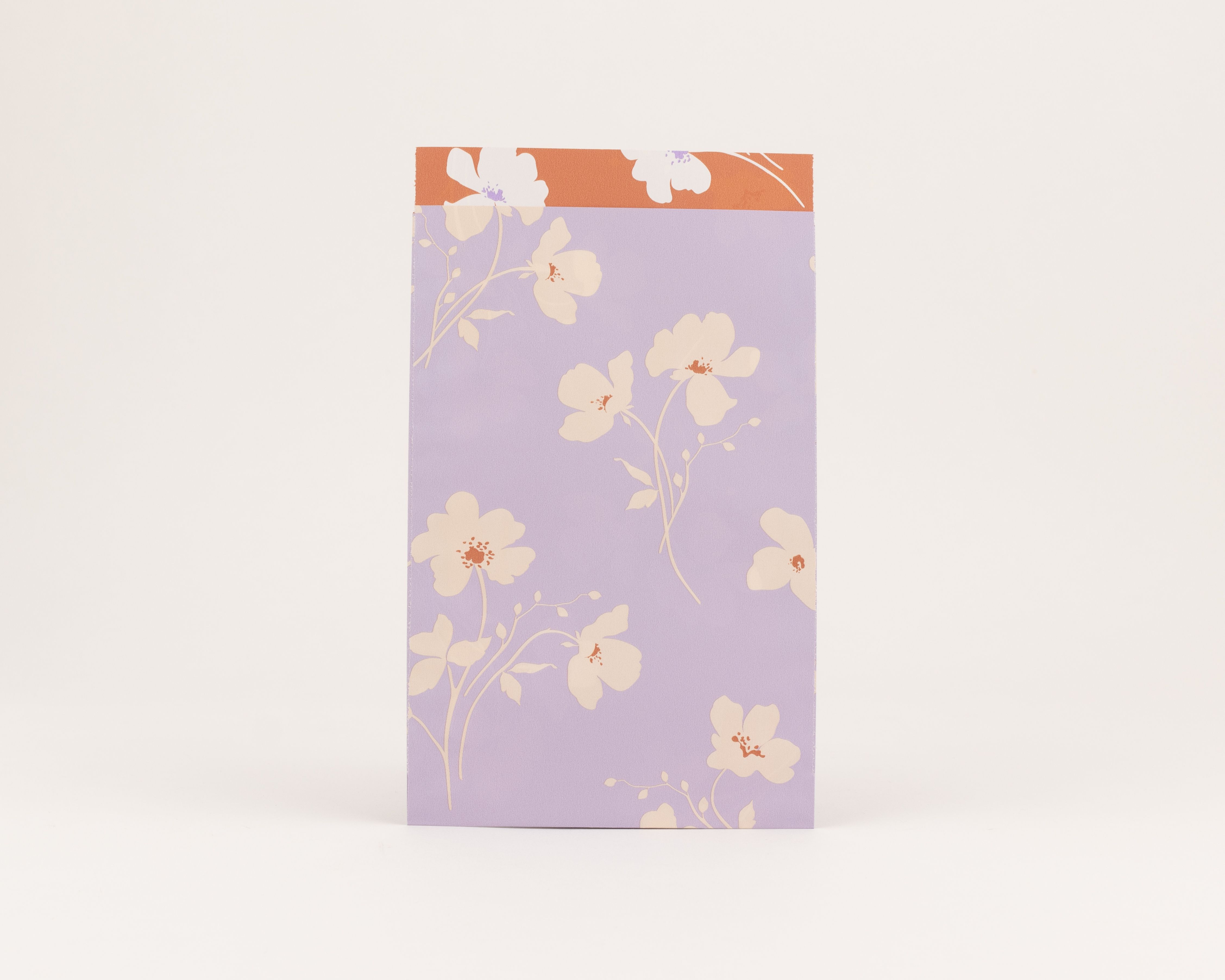 Flachbeutel mit Wiesenblütenmuster in Flieder und Beige, akzentuiert mit Rost. Die Innenseite ist rostfarben mit weißen Blüten