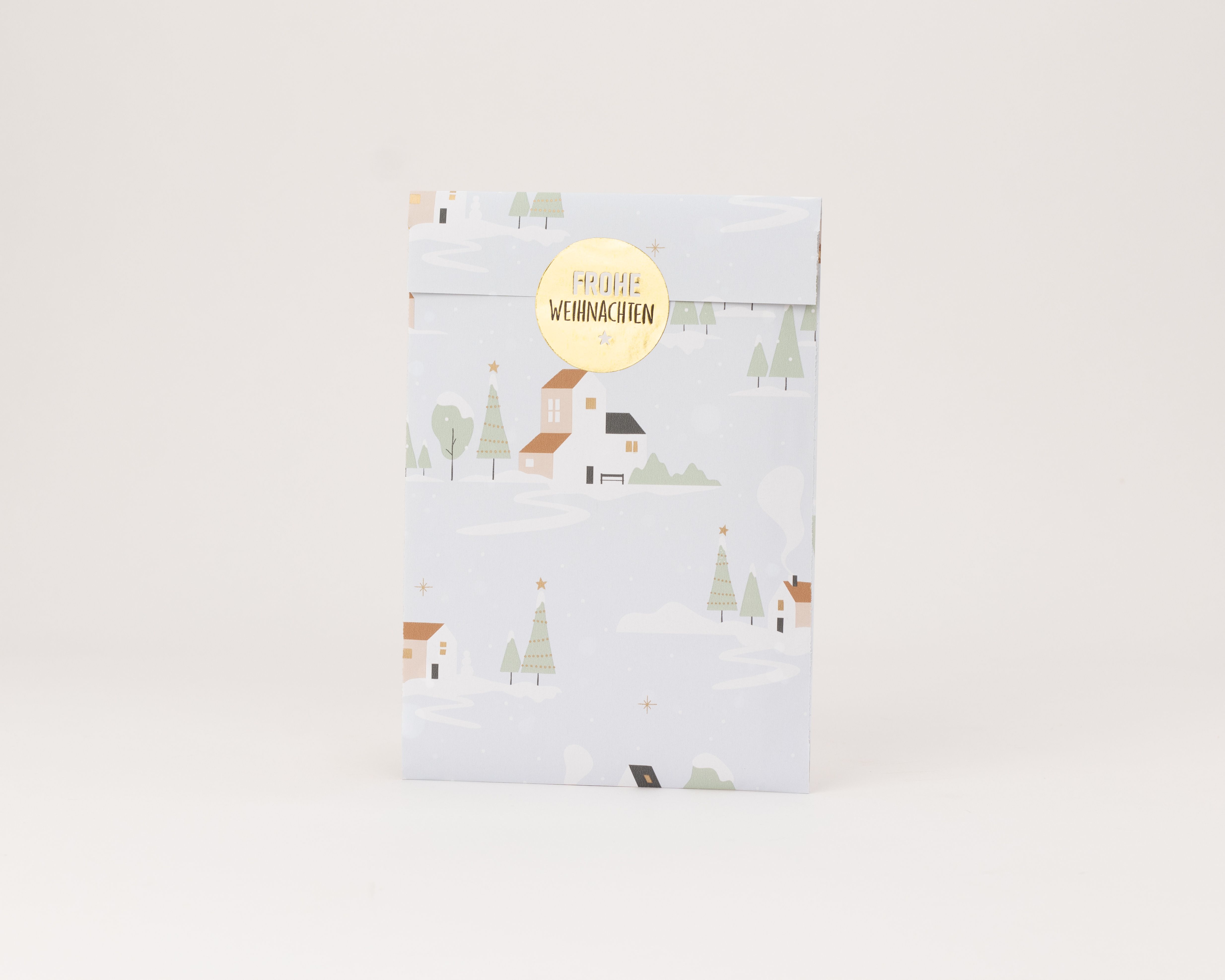 Flachbeutel mit winterlichem Dorfmotiv in Hellblau, darauf Häuser, verschneite Bäume und goldene Sterne mit Goldeffekt