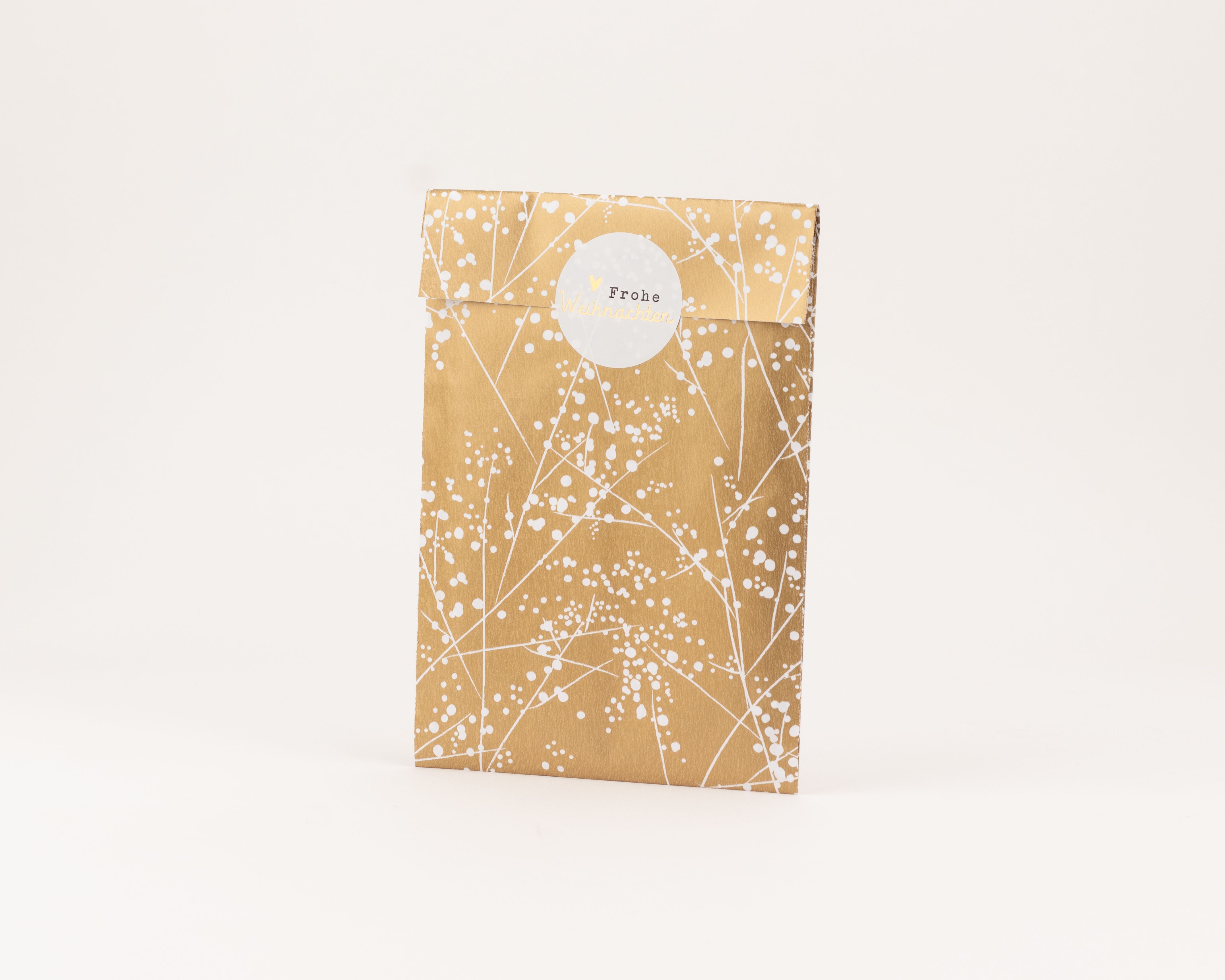 Flachbeutel in Gold mit weißem Winterfrost Muster und weißer Innenseite, verziert mit einem runden Aufkleber 'Frohe Weihnachten'