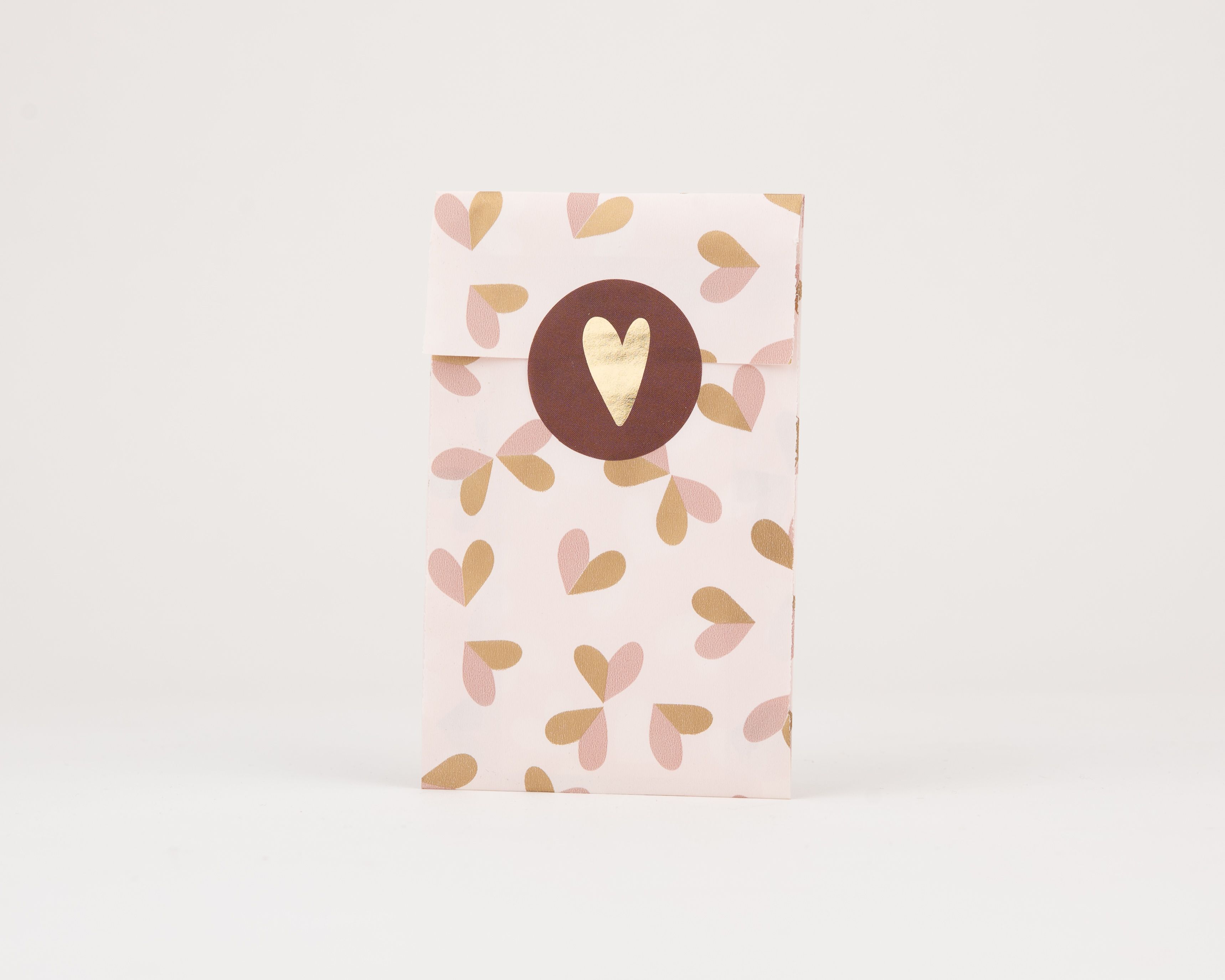 Papiertüten Flachbeutel mit einem Muster aus hellrosa und goldenen Herzen. Ein runder brauner Sticker mit goldenem Herz verschließt die Tüten