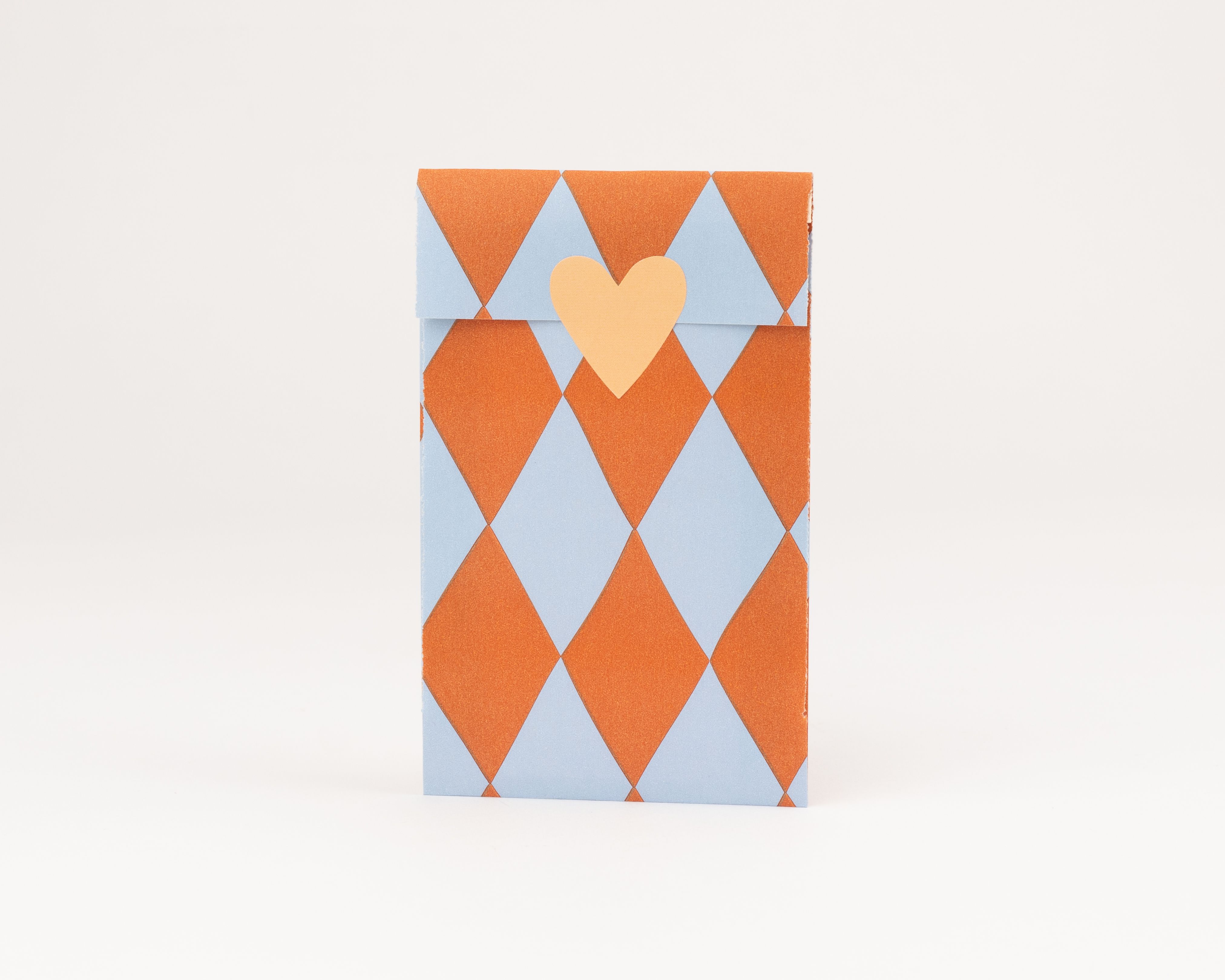 Flachbeutel mit rautenförmigem Muster in Hellblau und Orange, verziert mit einem pfirsichfarbenen Herz-Aufkleber
