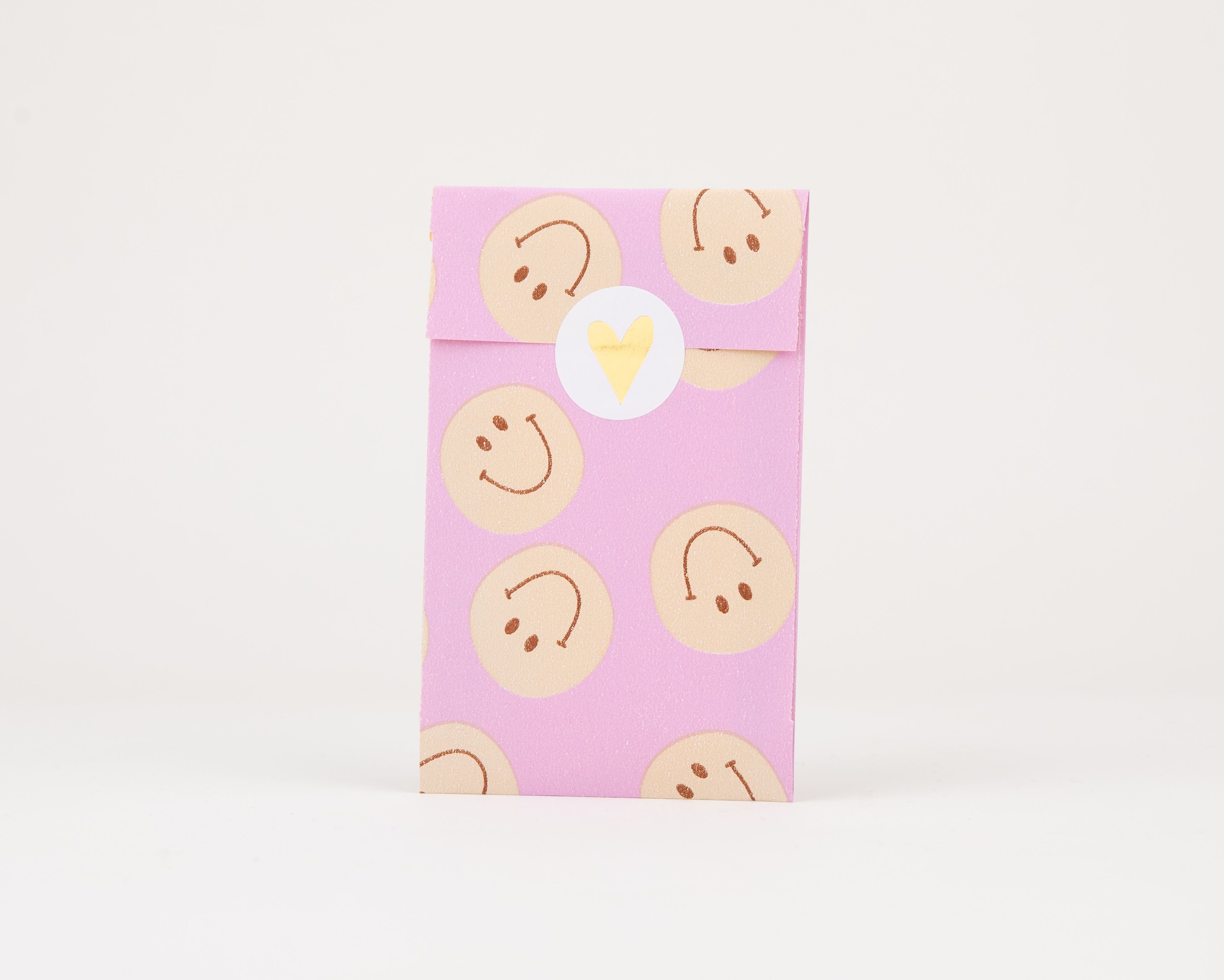 Papiertüten Flachbeutel mit Flieder als Hintergrundfarbe und orangen Smileys, die sichtbare Innenseite trägt dasselbe Muster