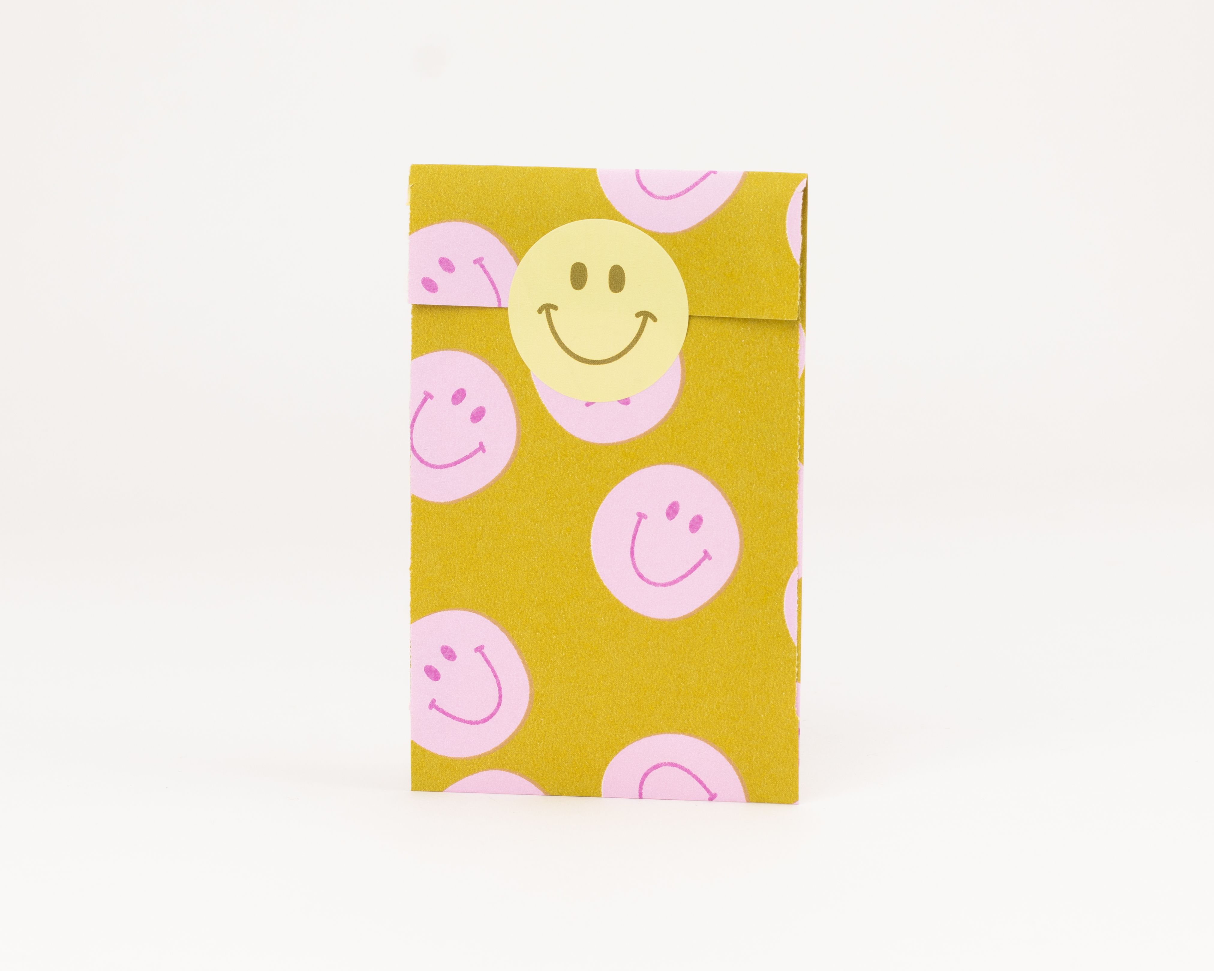 Flachbeutel mit gelbem Papier und rosa Smileys. Die Innenseite ist rosa. Ein gelber Smiley Aufkleber verschließt den Flachbeutel