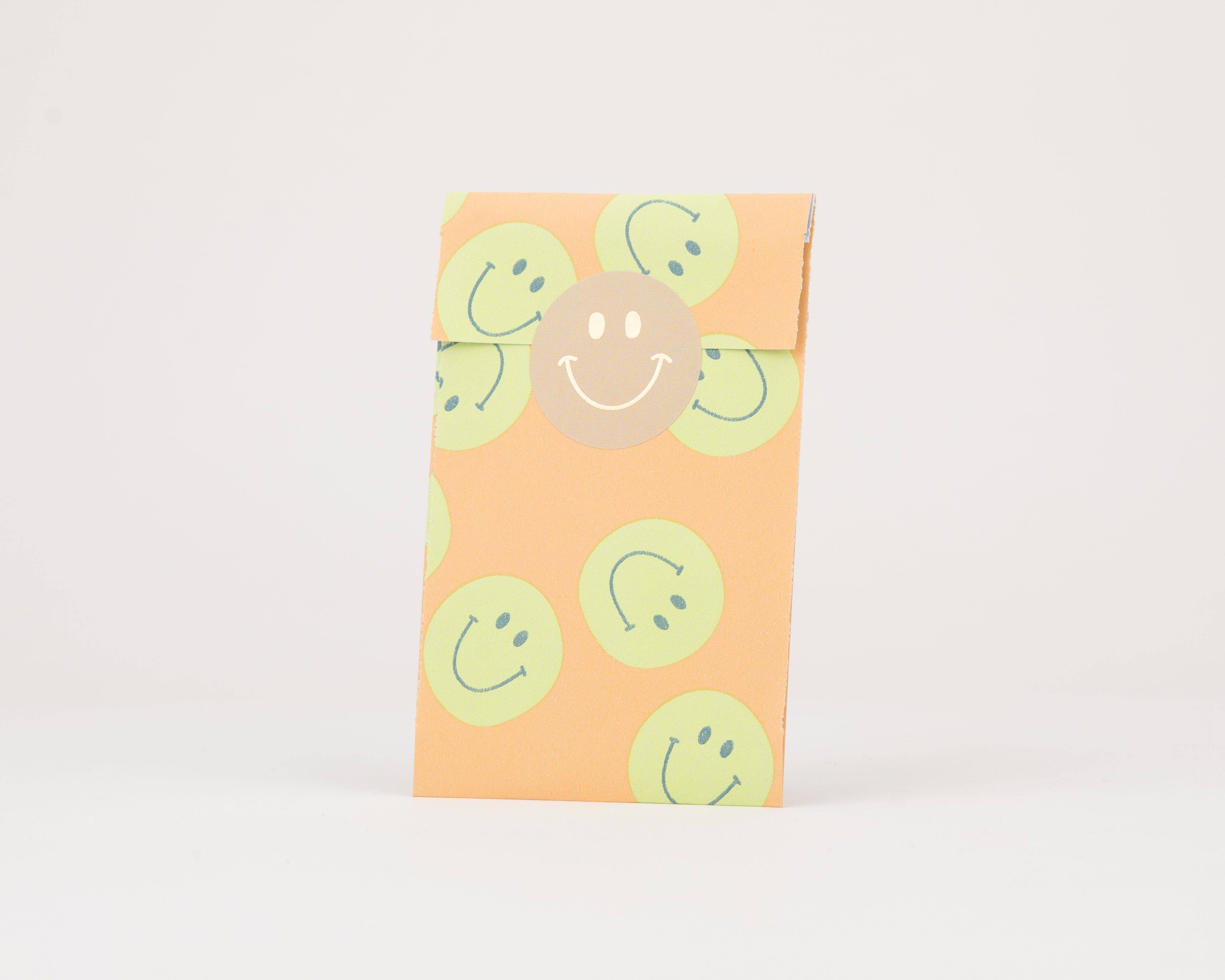 Papiertüten Flachbeutel in Orange mit einem Muster aus grünen Smileys und blauen Details. Die Innenseite ist ebenfalls orange