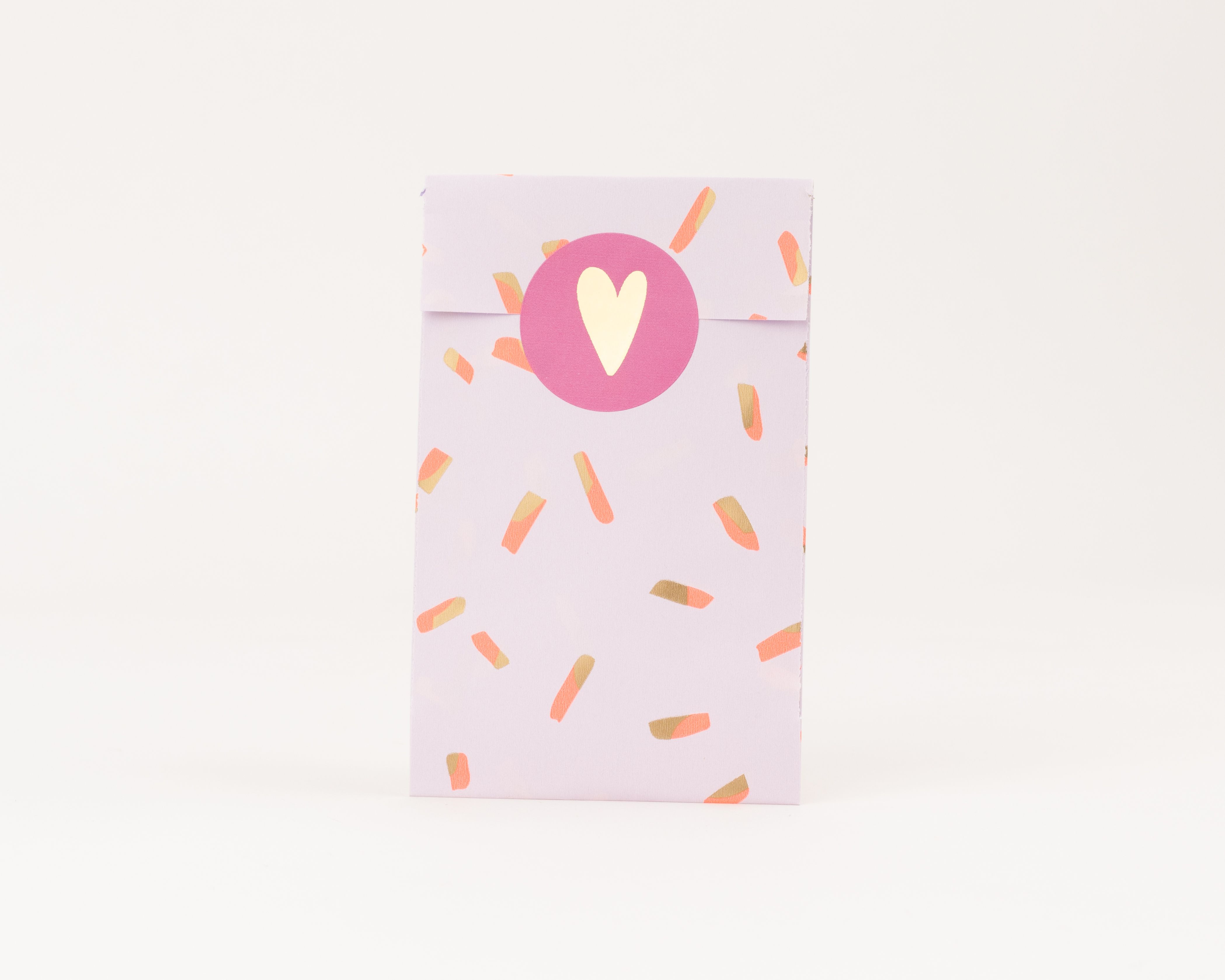 Flachbeutel mit hellfliederfarbenem Grund und Koralle-Gold-Sprinkles-Muster, versiegelt mit einem runden Sticker und Goldherz
