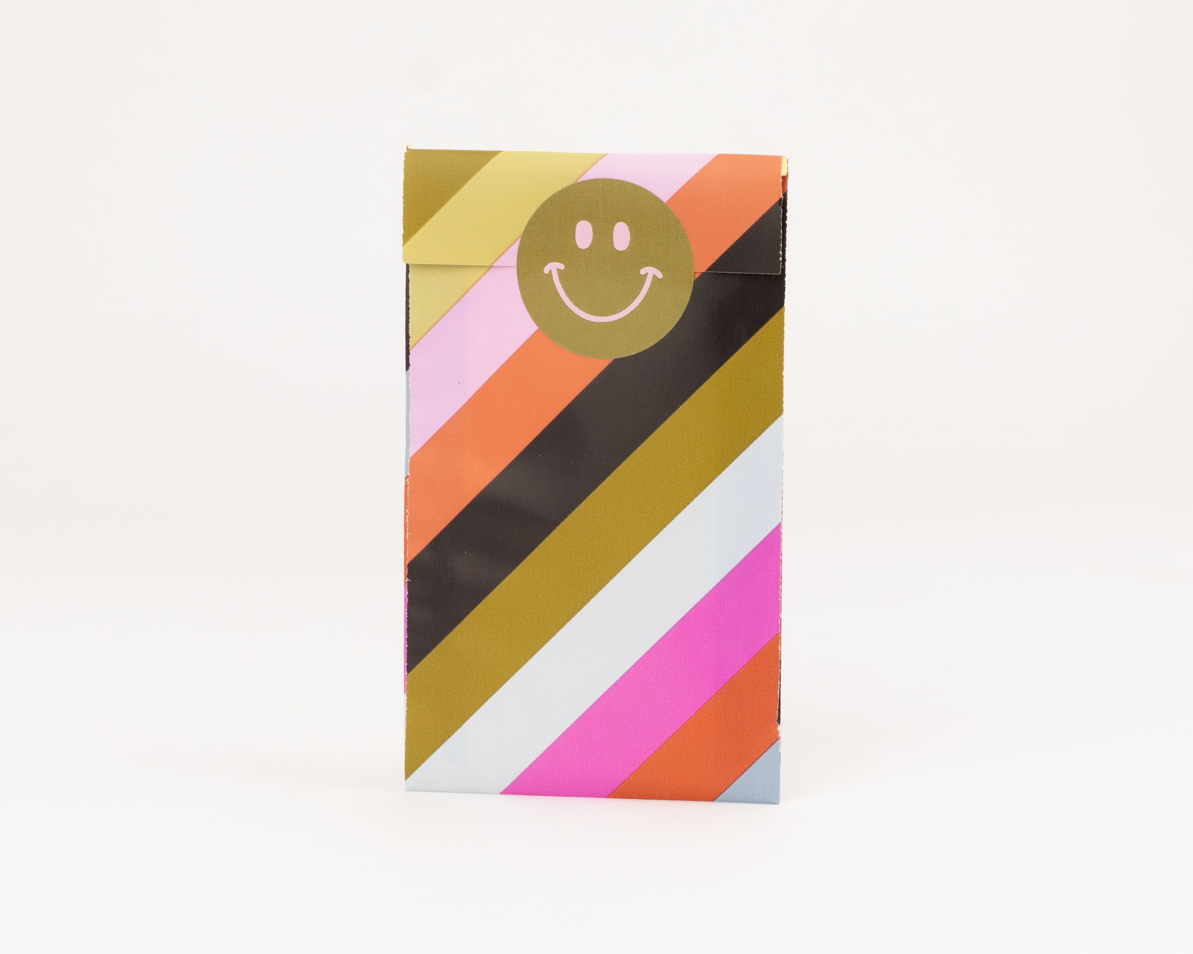 Papiertueten mit bunten diagonalen Streifen in Gold, Pink, Orange, Schwarz und Weiß, verziert mit einem goldenen Smiley-Gesicht. Die Innenseite ist hellblau-grau