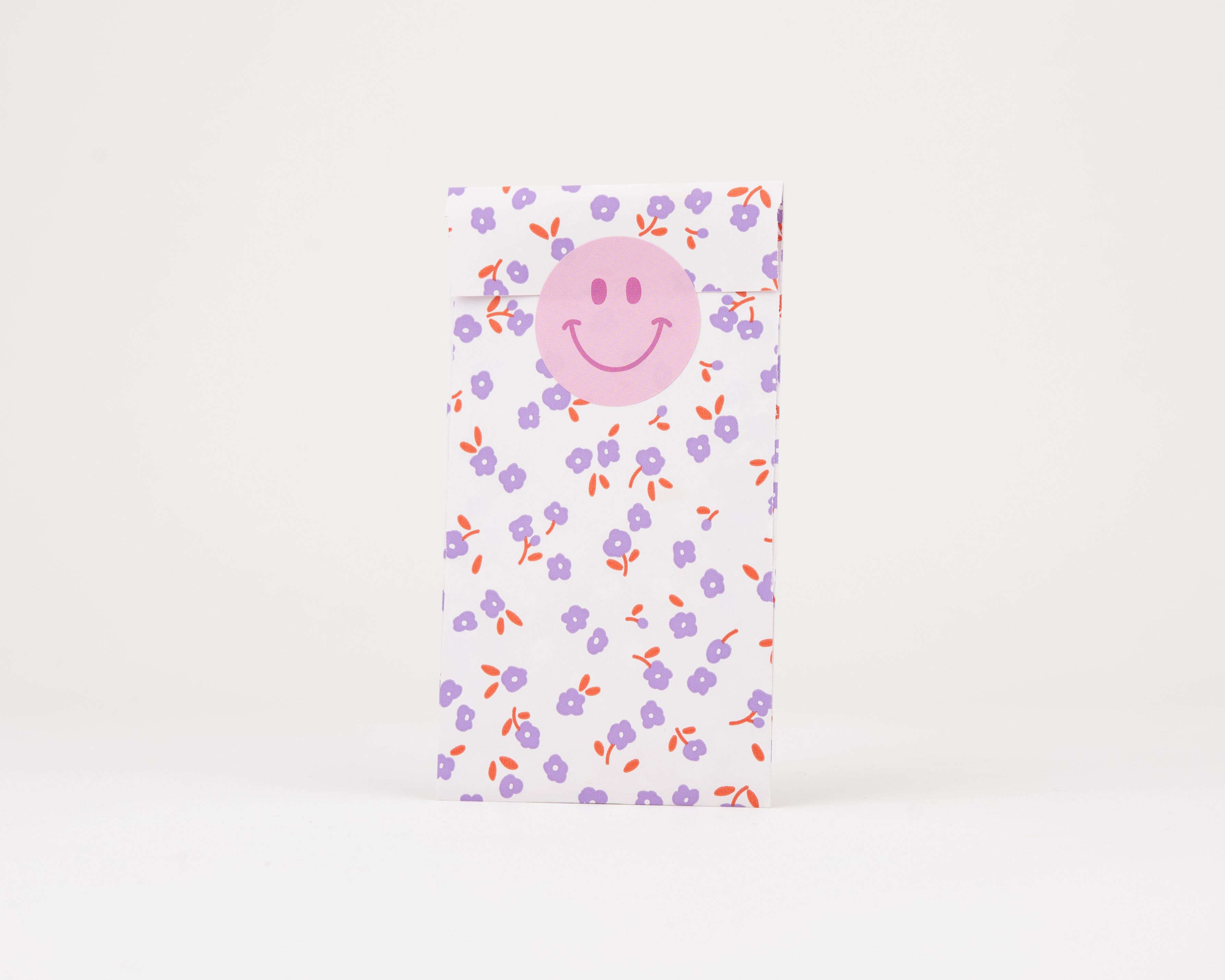 Papiertüten Flachbeutel mit floralem Blumenmuster in Flieder, Hellflieder und Rost. Ein Smiley-Sticker und die passende Innenseite sind sichtbar