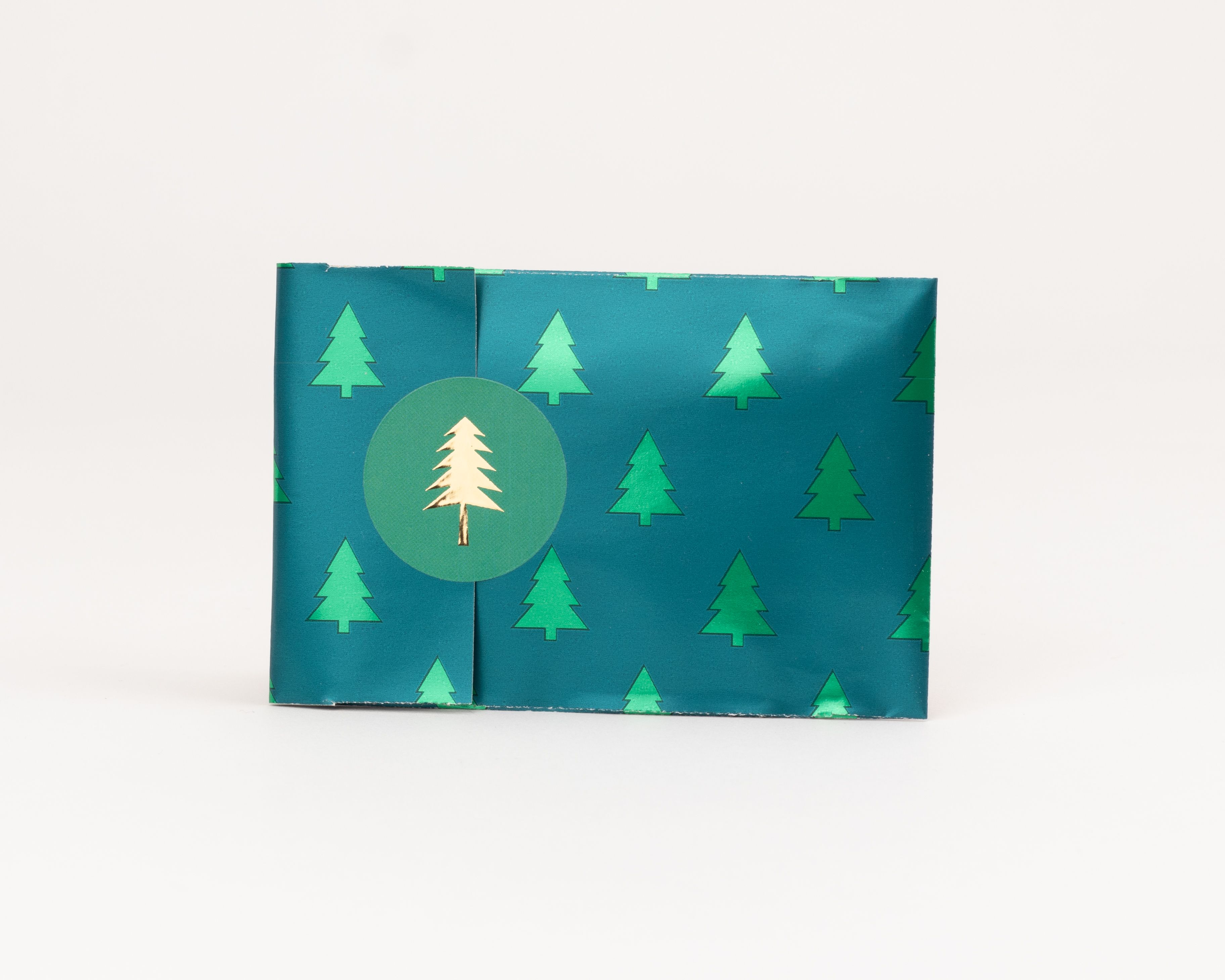 Flachbeutel mit dunkelgruener Außenseite und hellgruener Innenseite, verziert mit einem Tannenbaum-Muster und einem goldenen Tannenbaum-Aufkleber