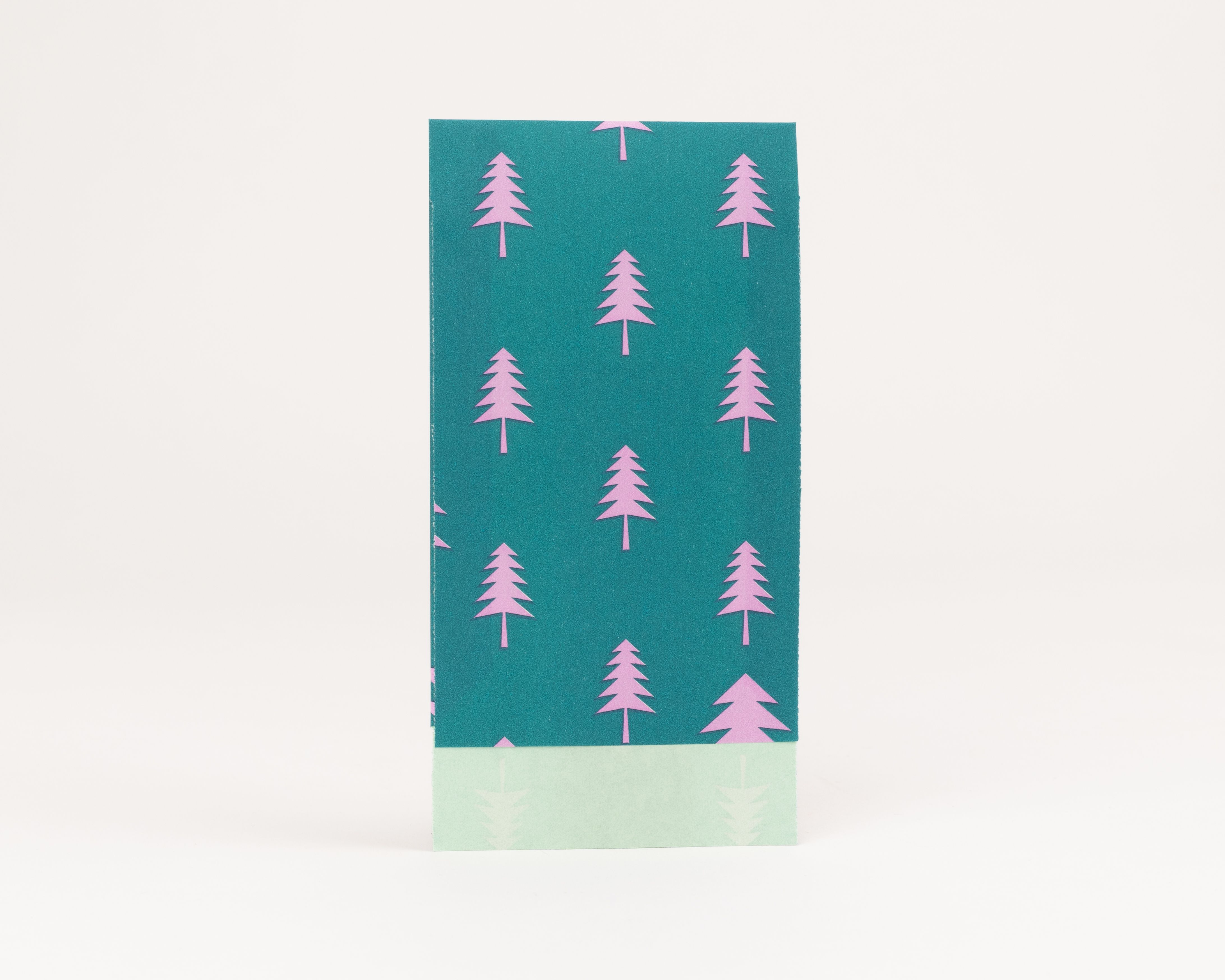 Flachbeutel mit dunkelgrünem Hintergrund und pinkfarbenen Tannenbaummotiven. Die sichtbare Innenseite ist hellgrün mit dezenten Tannenmustern