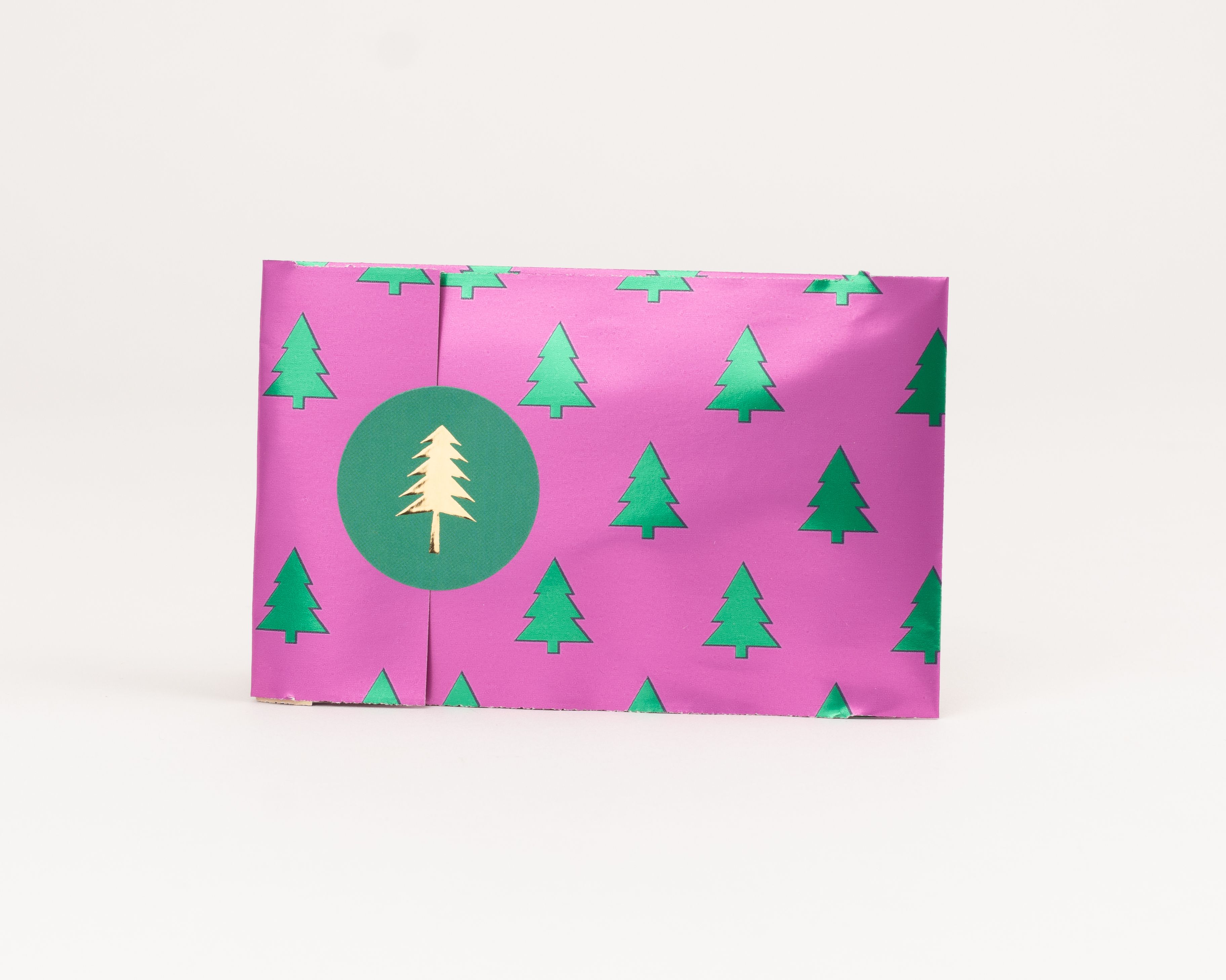 Flachbeutel in Pink mit grünen Tannenbäumen als Muster und einem runden grünen Aufkleber mit goldenem Tannenbaummotiv Die Innenseite ist grün