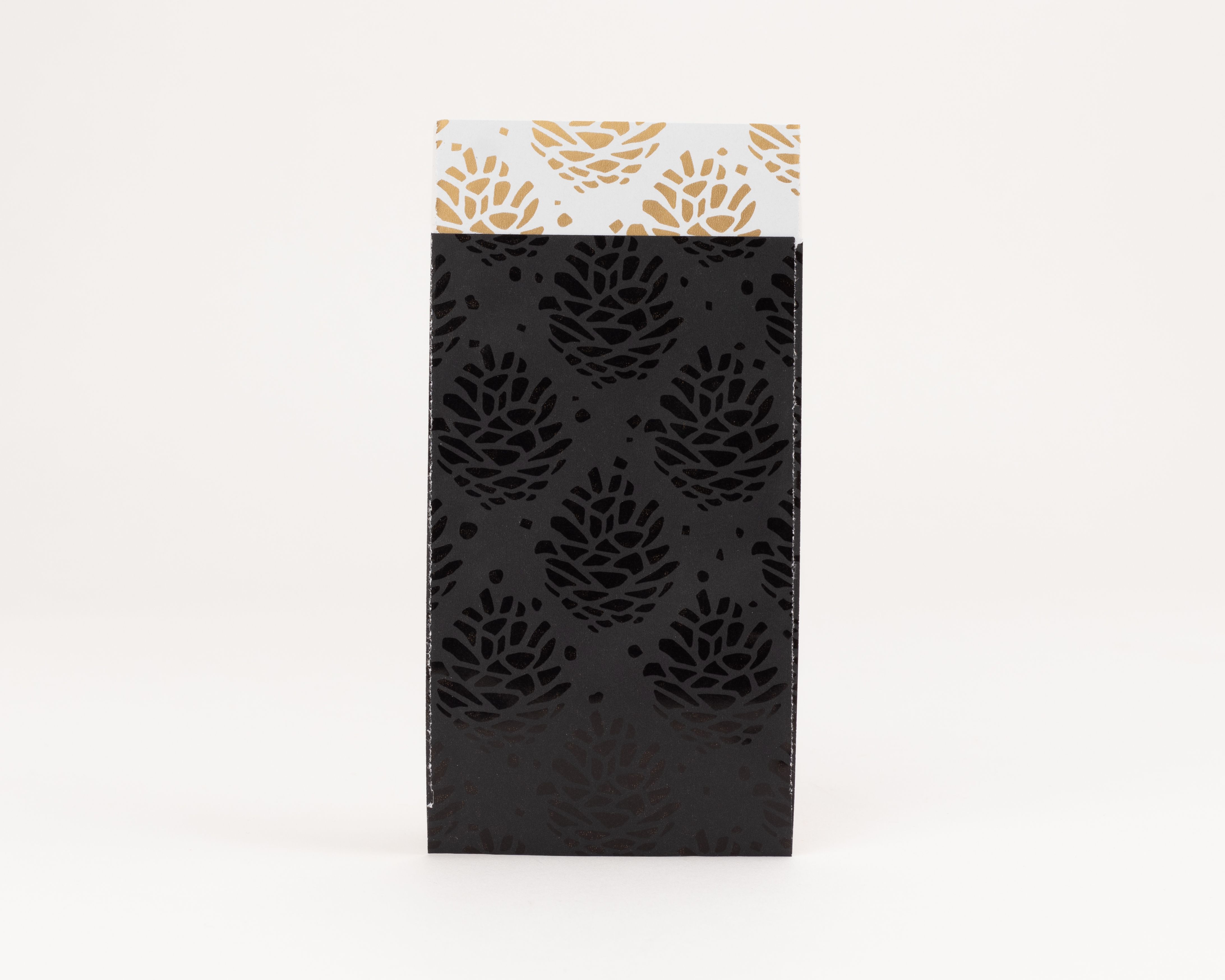 Flachbeutel in mattem Schwarz mit glänzenden Tannenzapfen und goldenen Akzenten, die Innenseite ist weiß mit goldenem Tannenzapfenmuster