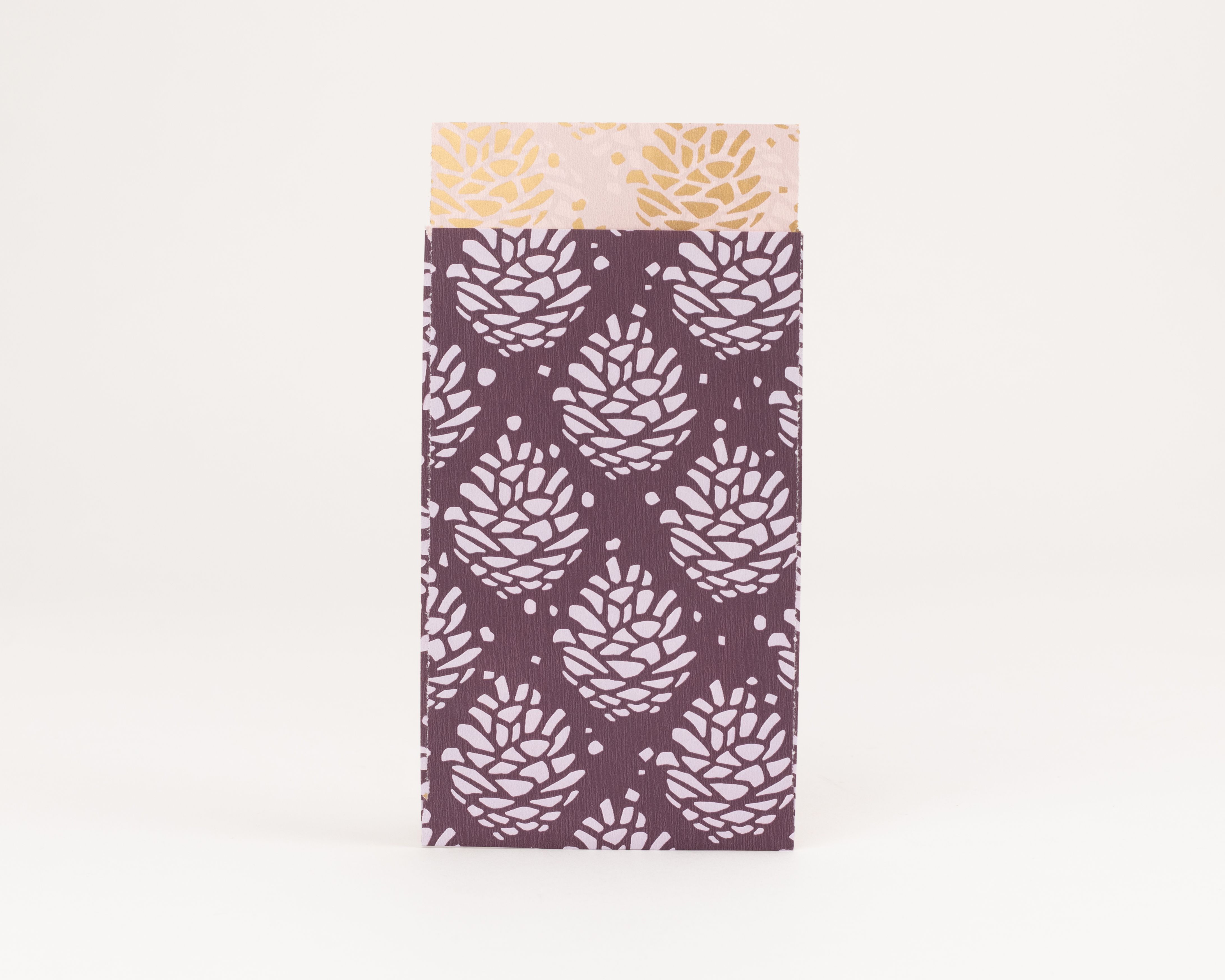 Flachbeutel in Violett mit hellviolettem Tannenzapfen-Muster. Die Innenseite ist Rosa mit goldenen Zapfenmotiven