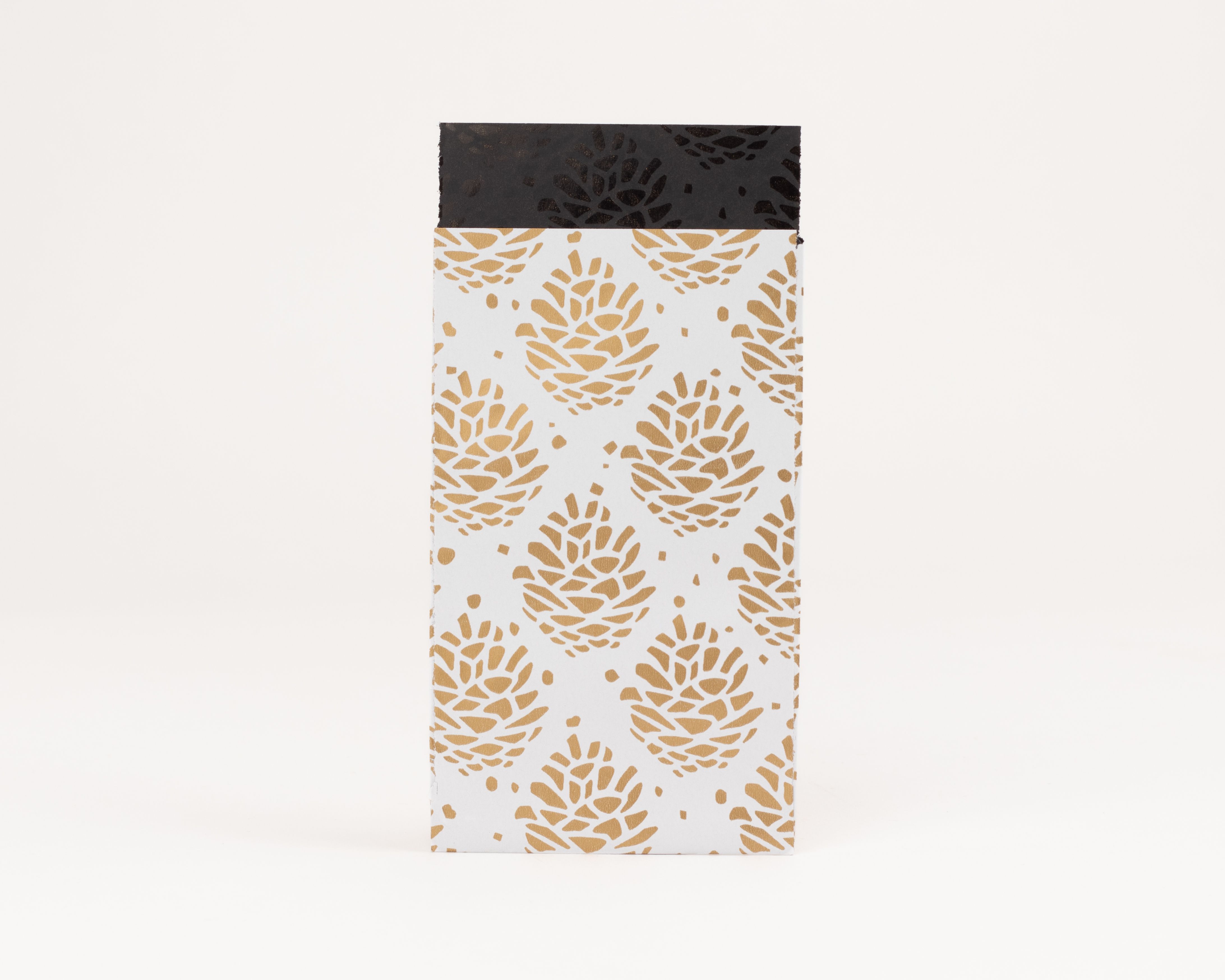 Flachbeutel mit goldbraunem Tannenzapfenmuster auf weißer Oberfläche und Innenseite in Schwarz mit dunklem Motiv