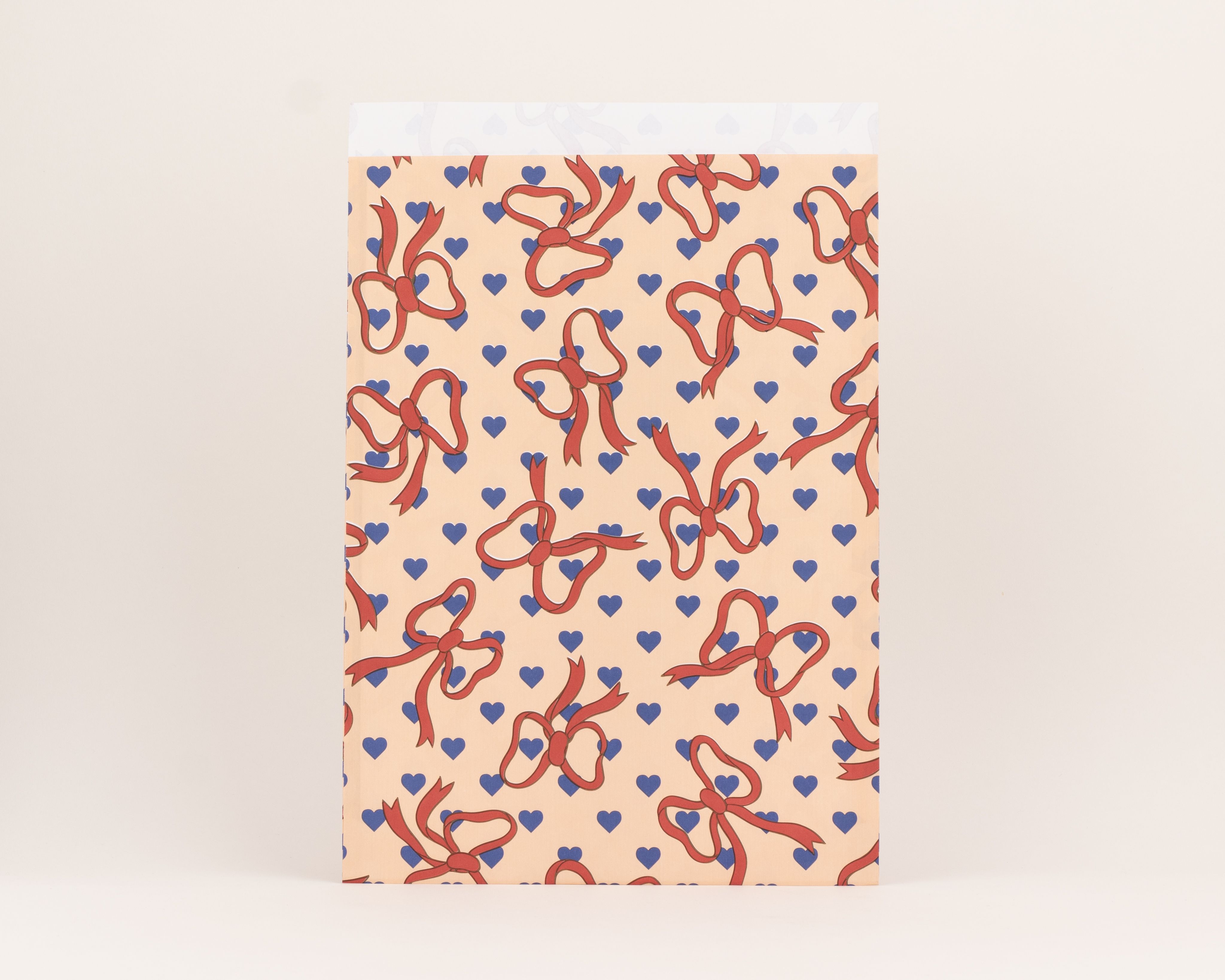 Flachbeutel mit Pfirsich-Hintergrund, roten Schleifen und kornblumenblauen Herzen. Die Innenseite zeigt helle, schwache Muster