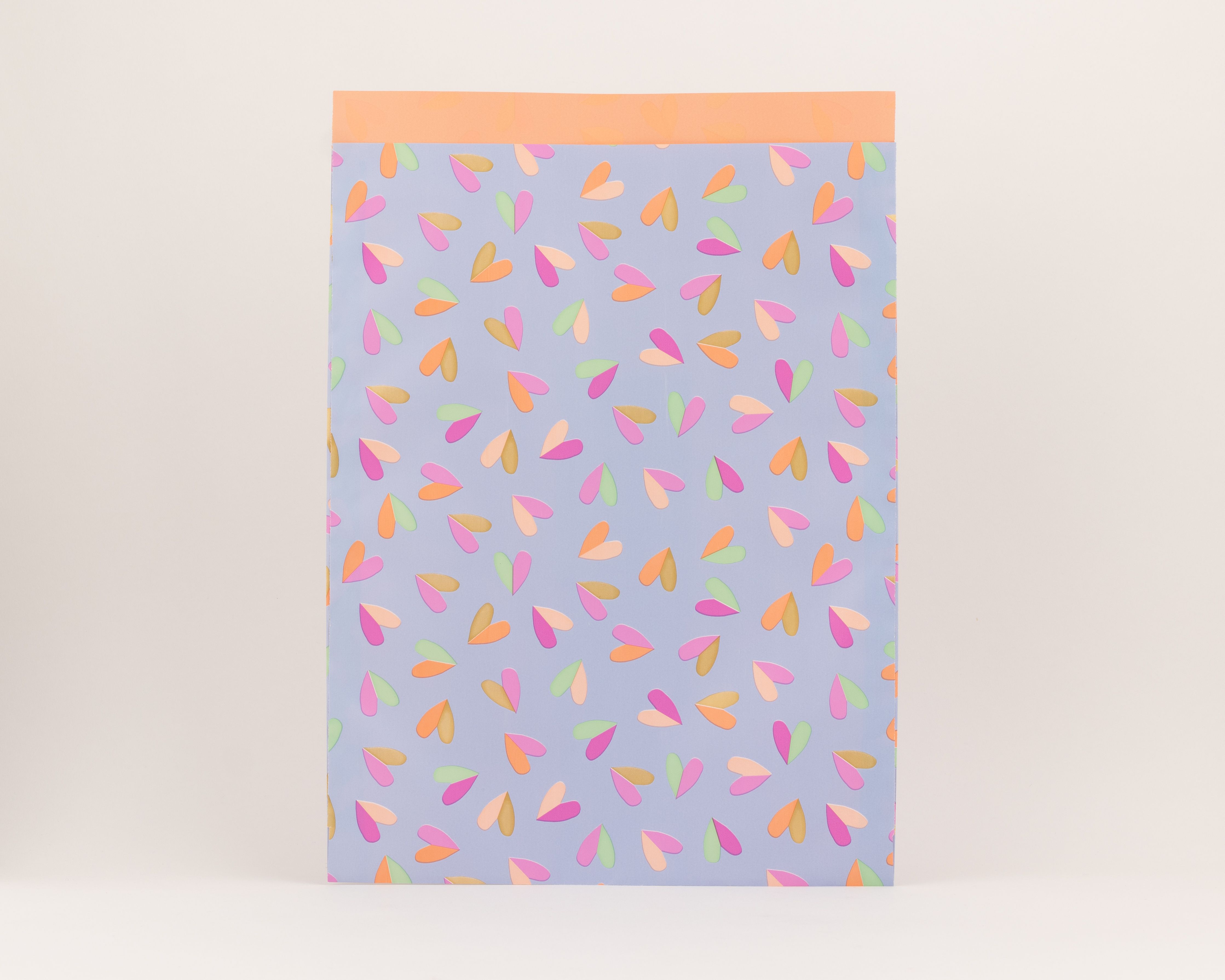 Flachbeutel mit blauem Hintergrund und einem Herzflatter-Muster in den Farben Pink, Grün, Orange und Gold. Die Innenseite ist einfarbig Orange