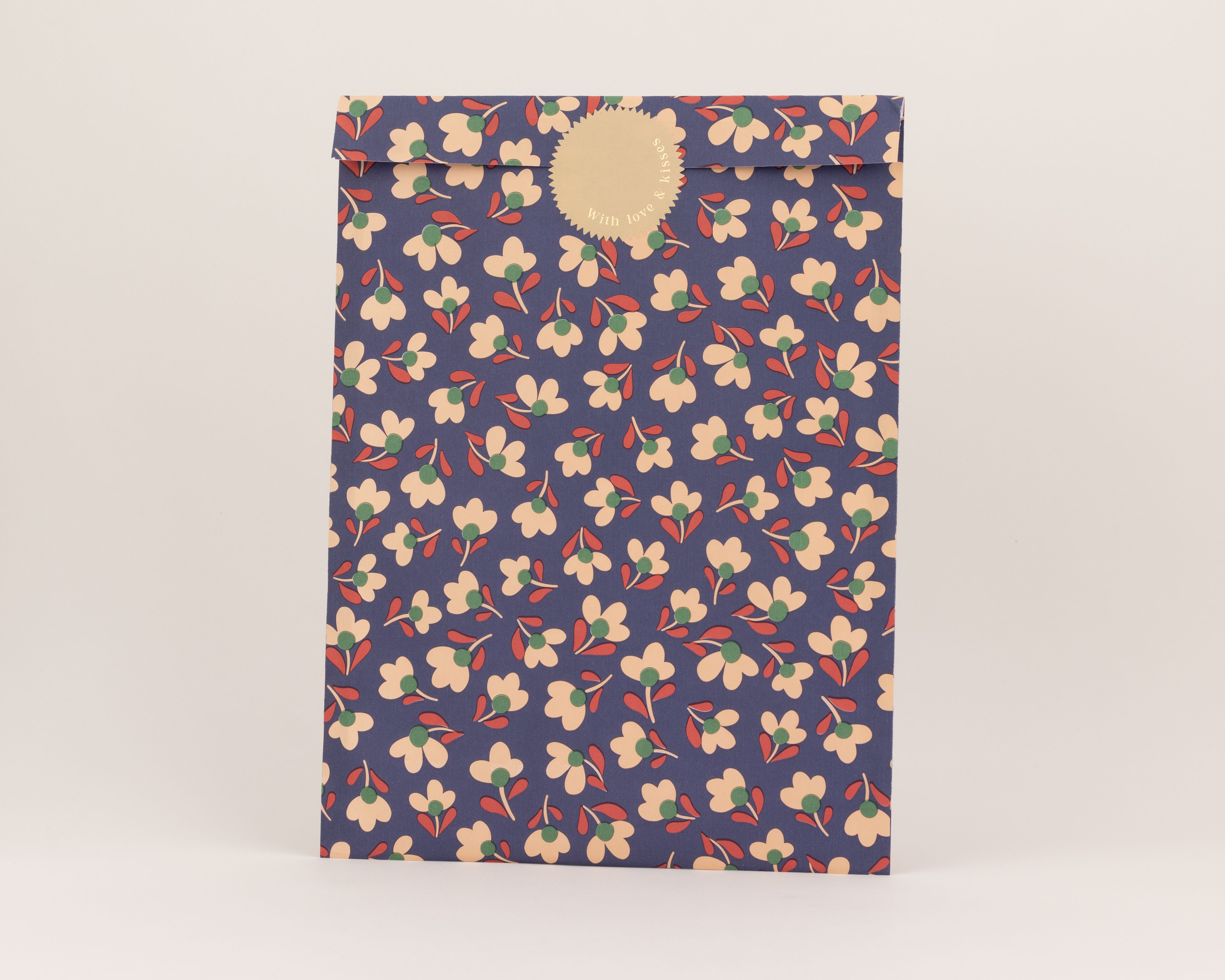 Flachbeutel mit dunkelblauer Außenseite und floralem Muster: beige Blüten, grüne Zentren, rote Stiele. Innenseite hellbeige