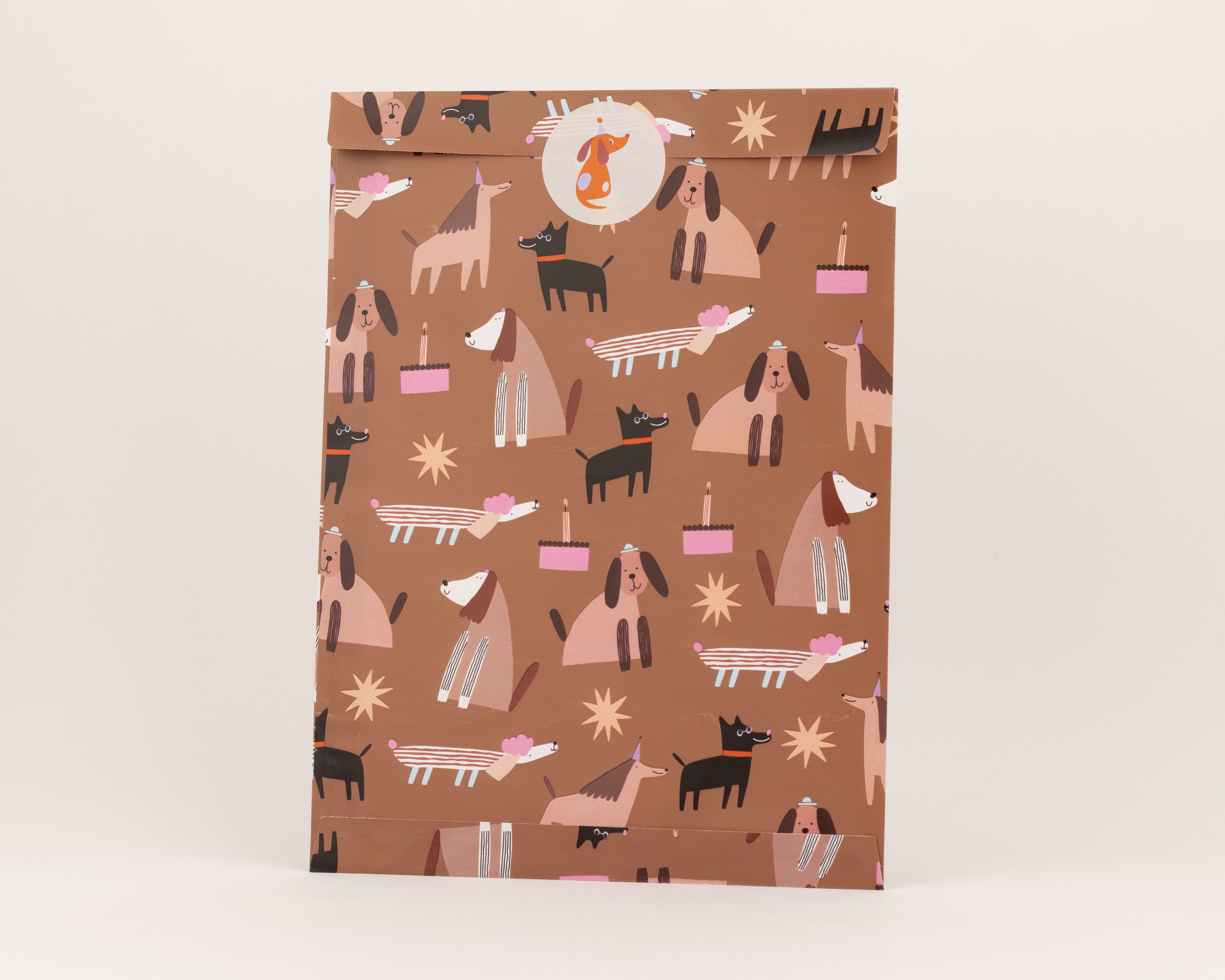 Flachbeutel mit braunem Hintergrund und einem Muster aus Hunden in Beige und Schwarz mit pinken Torten und Sternen