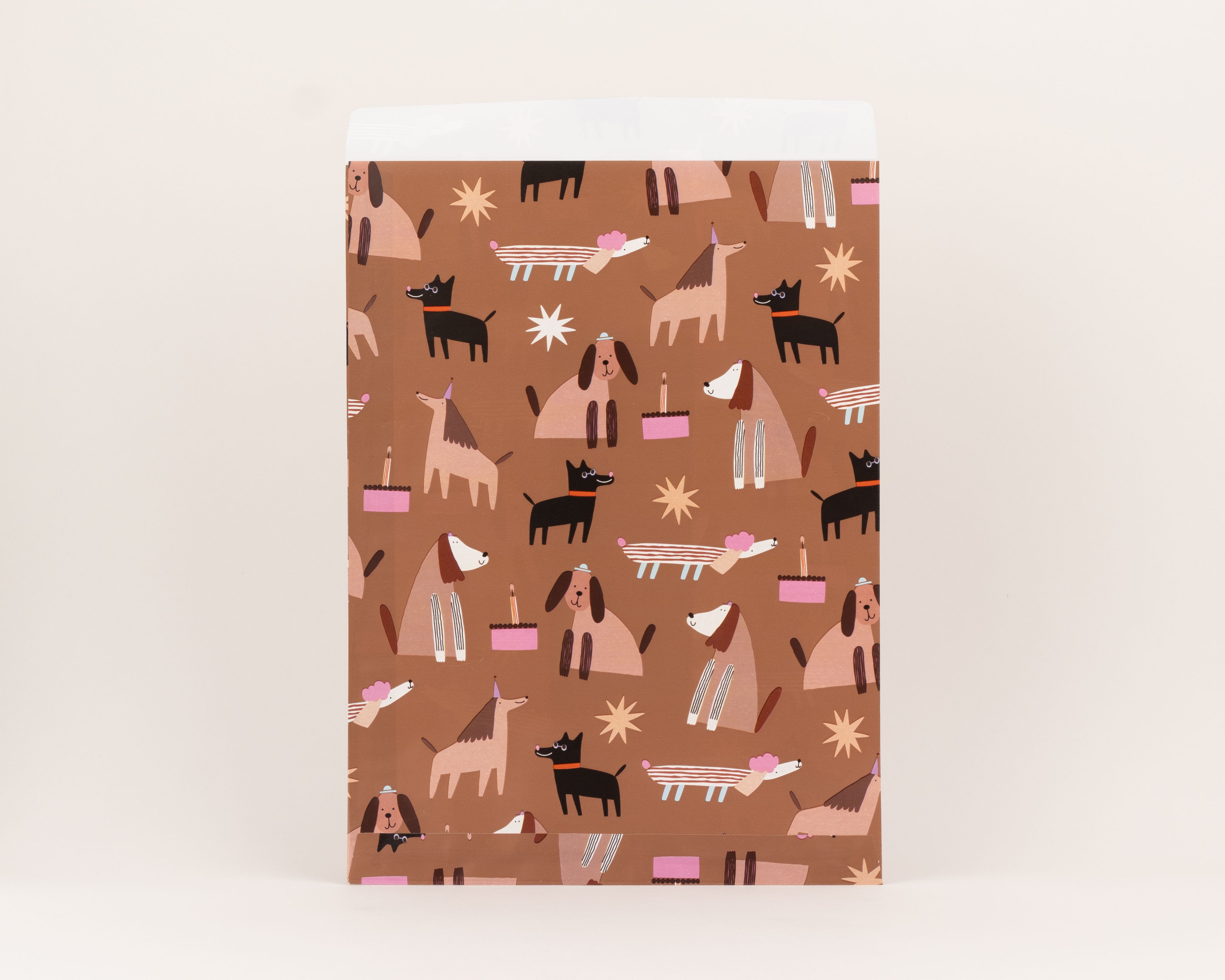 Flachbeutel mit brauner Außenseite, verziert mit Hunden in Beige und Schwarz, rosa Geburtstagstorten und Sternen. Die Innenseite ist Beige