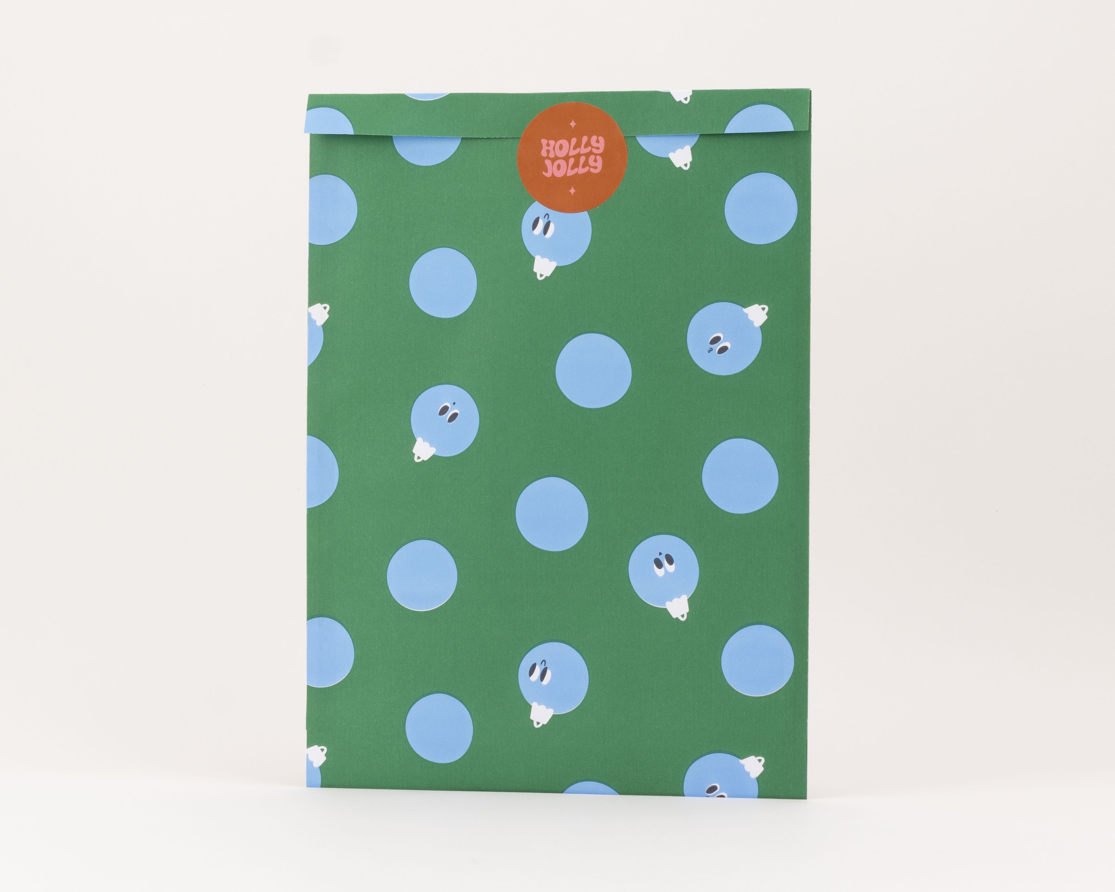 Flachbeutel mit grünem Hintergrund und blauen Peek-a-Boo Baubles. Die Innenseite ist blau und ein orangefarbener Holly Jolly Aufkleber ist sichtbar