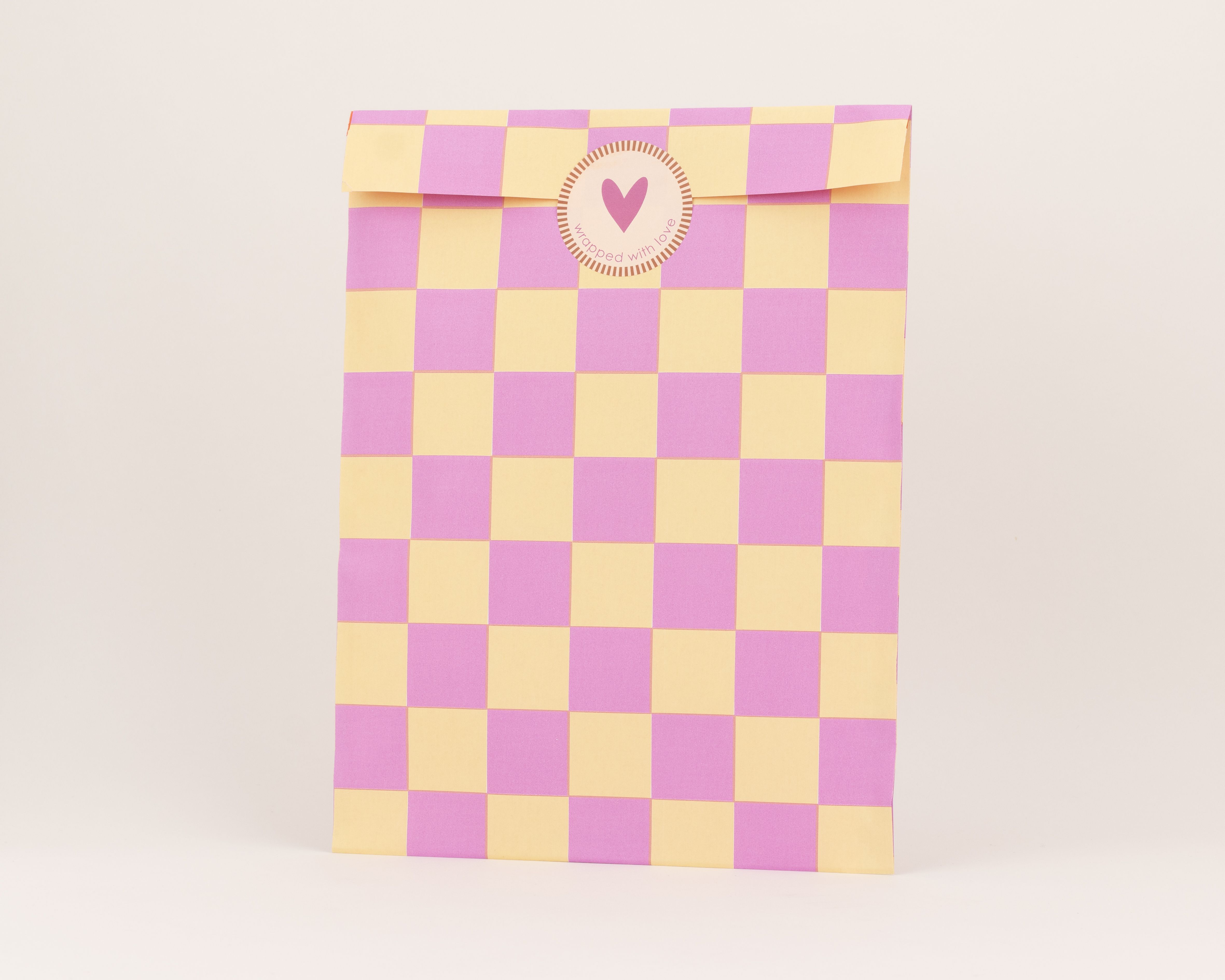 Flachbeutel mit auffälligem Schachbrettmuster in Pink und Gelb, die Innenseite des Umschlags ist einfarbig Orange