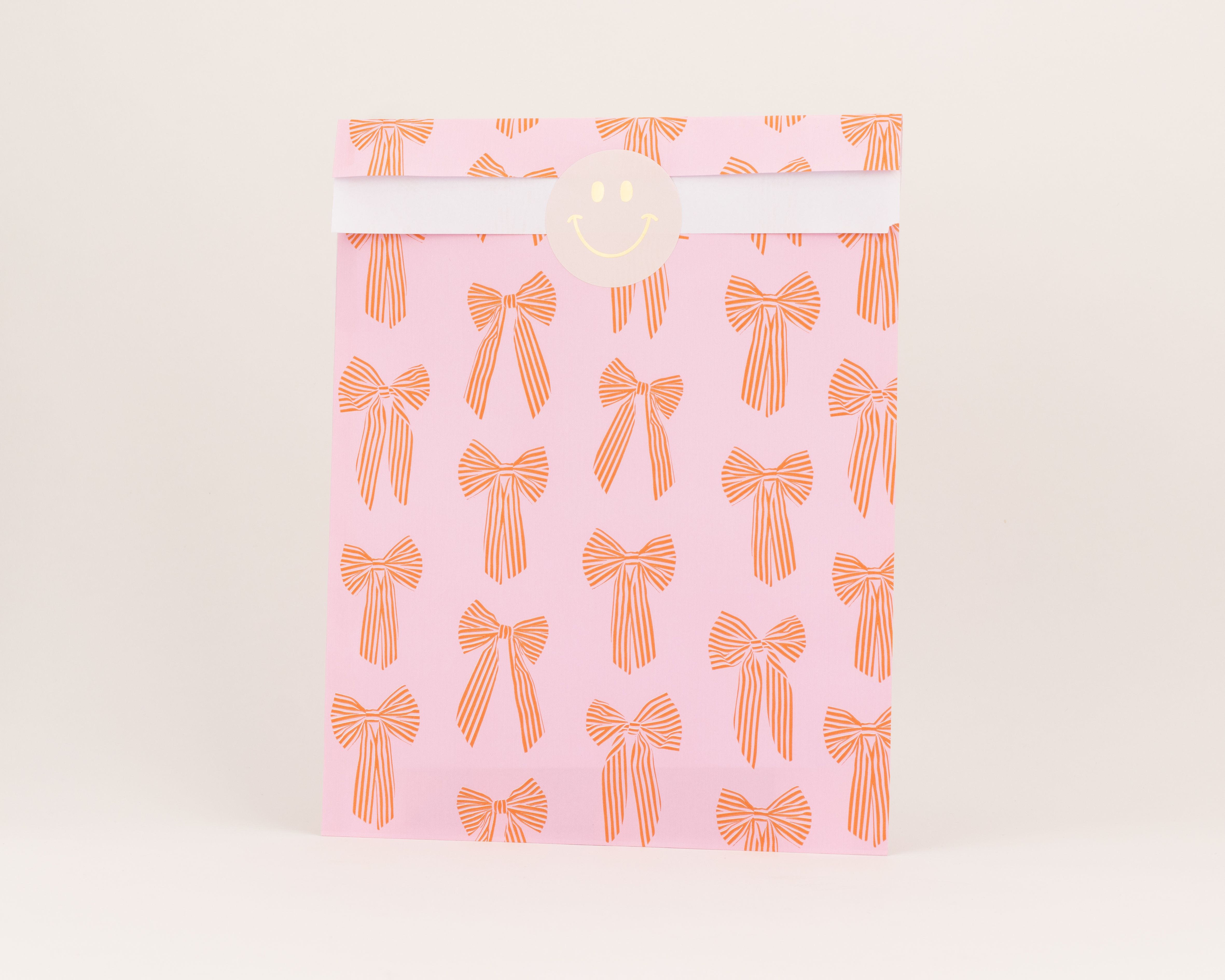 Flachbeutel mit rosa Hintergrund und wiederholtem roten Schleifenmuster. Die Innenseite des Beutels ist weiß.