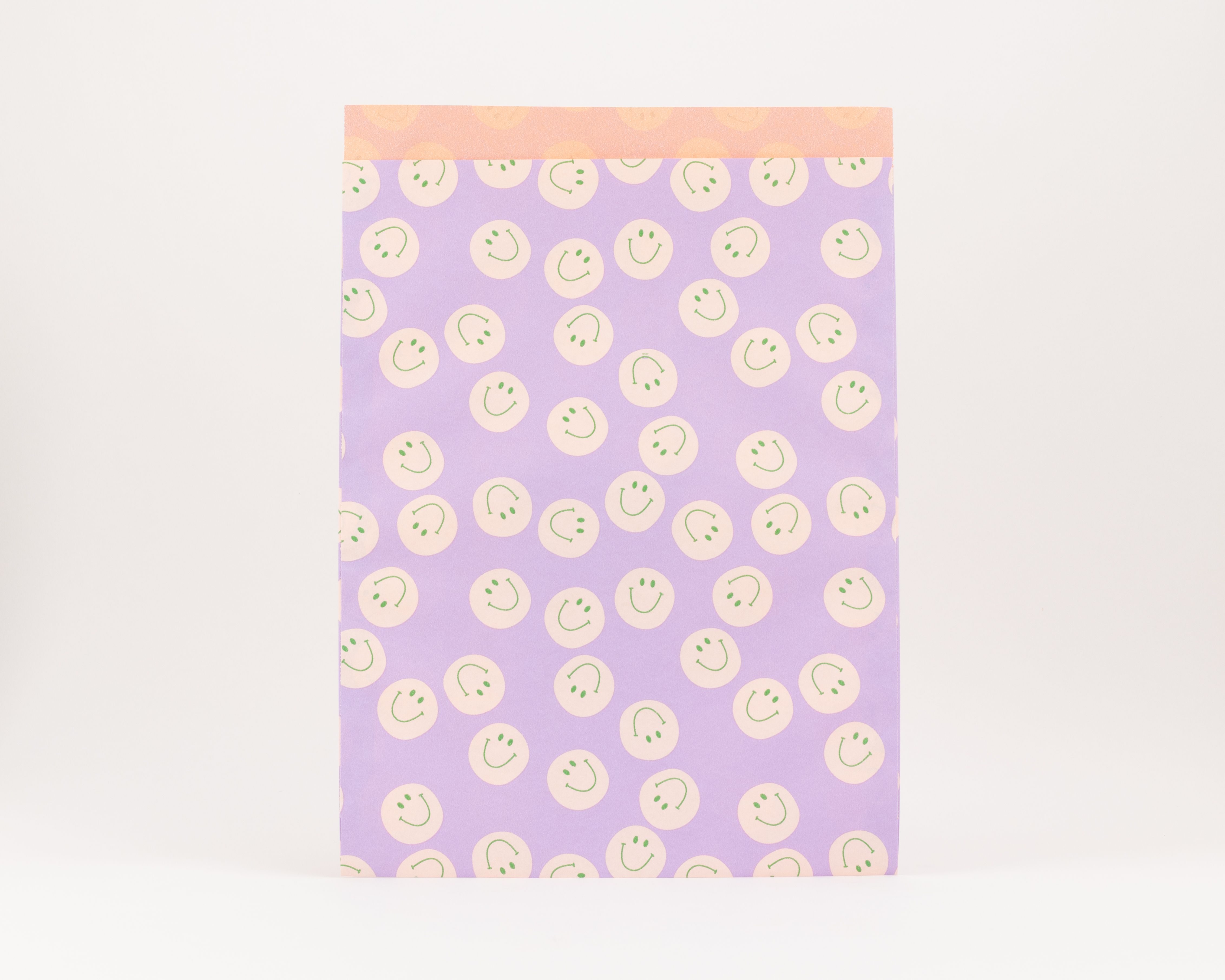 Flachbeutel in Fliederfarbe mit einem durchgehenden Muster aus Elfenbein Smileys und grünen Gesichtern. Die Innenseite hat ein Wellenmuster
