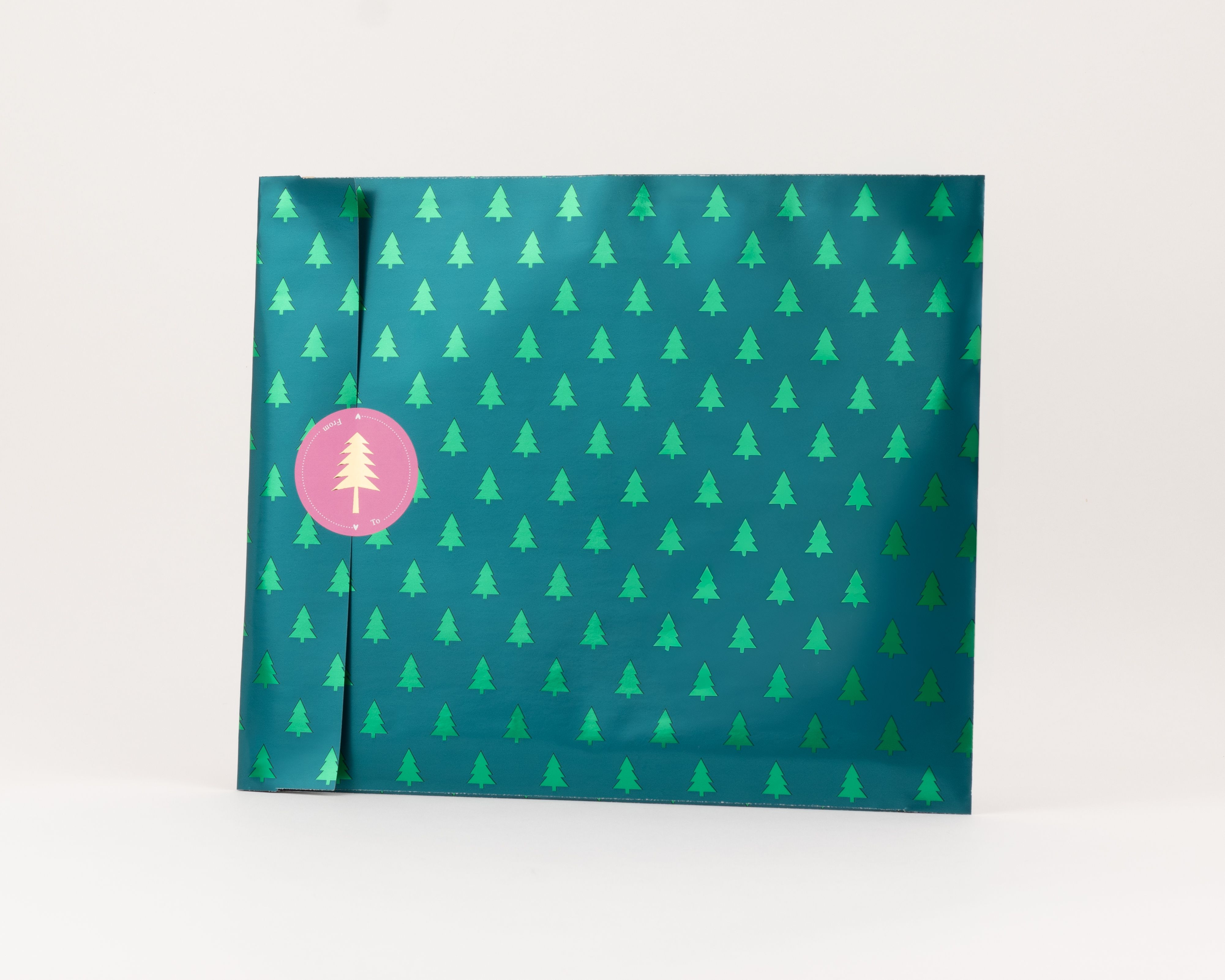 Flachbeutel mit grünem Grund und wiederholendem Muster aus metallic glänzenden Tannenbäumen, die Innenseite ist beige