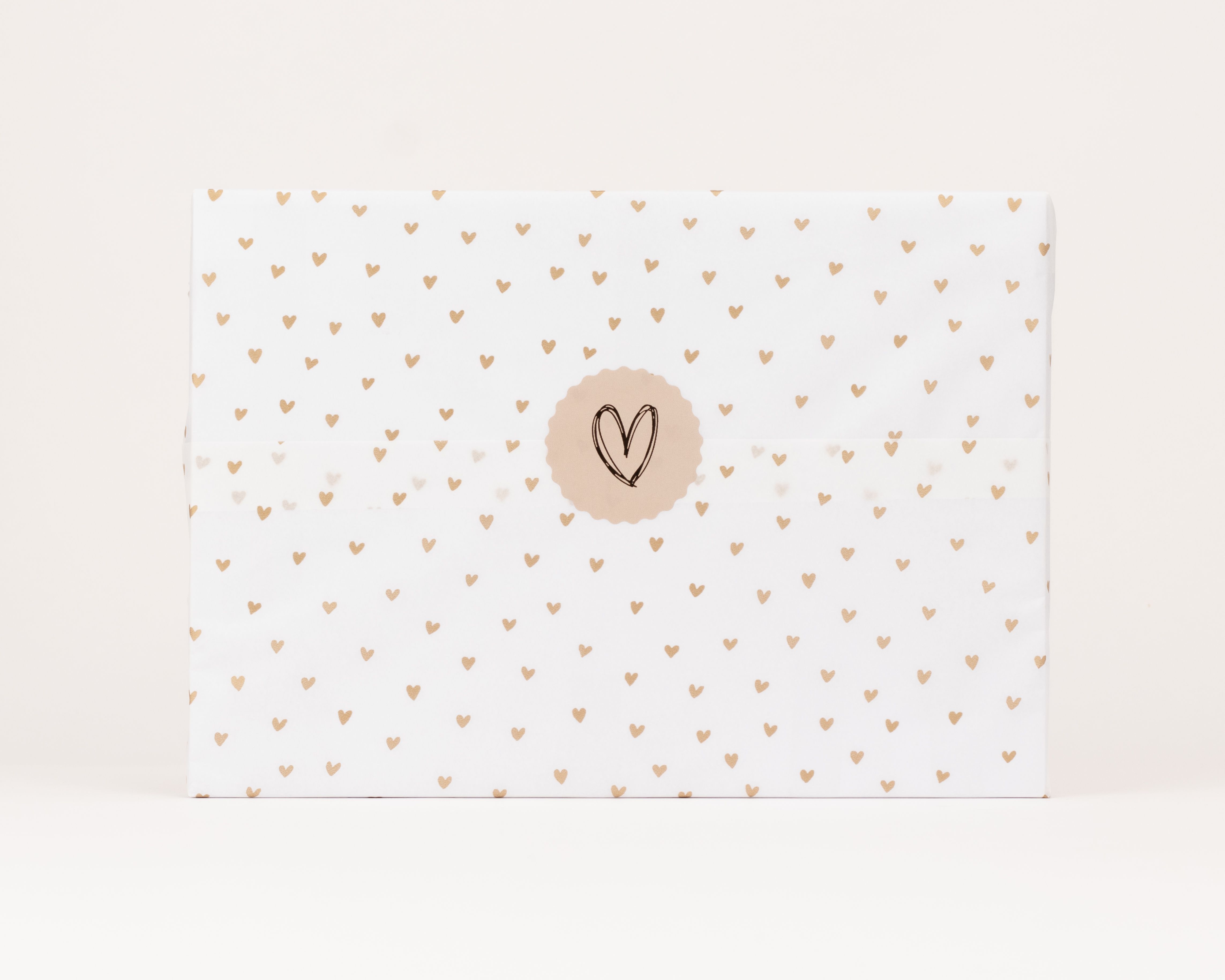 Seidenpapier weisses mit goldenen Herzchen gemustertes Darauf ein runder hellbrauner Aufkleber mit gezeichnetem Herz