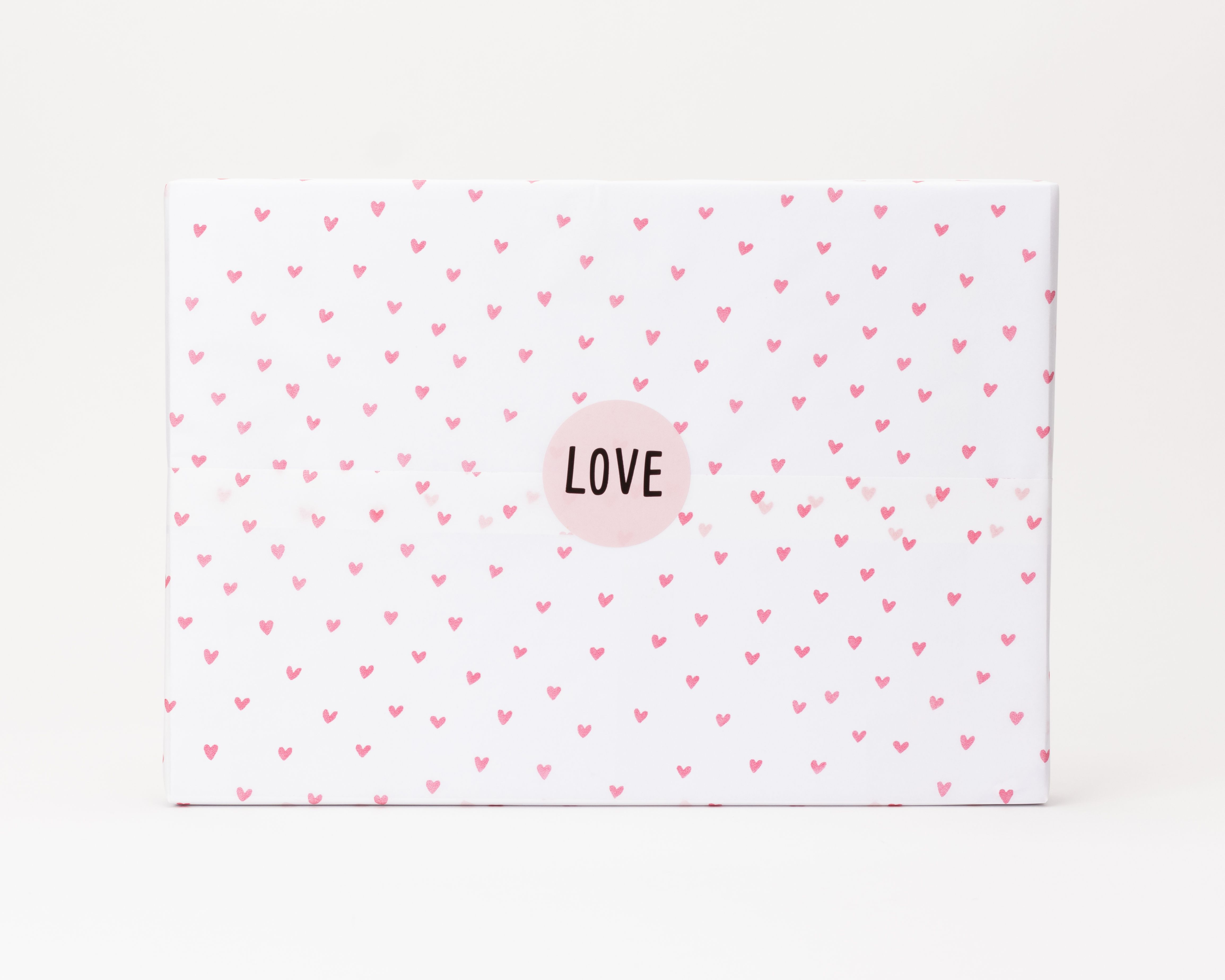 Seidenpapier weiß mit pinken Herzen Muster. Darauf ein runder hellpinker Aufkleber mit LOVE Text