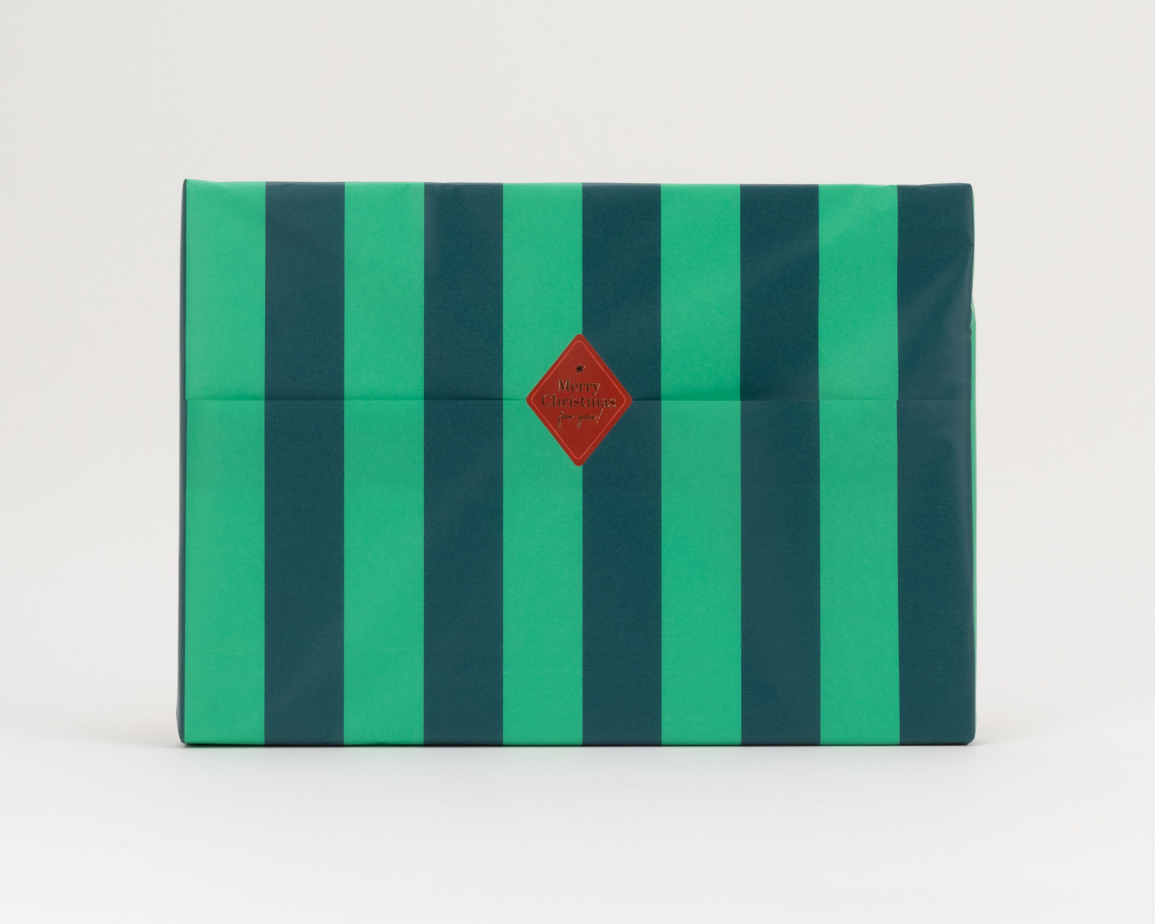 Seidenpapier mit breiten Blockstreifen in Grün und Dunkelgrün. Darauf ein roter, rautenförmiger Aufkleber mit goldener Schrift