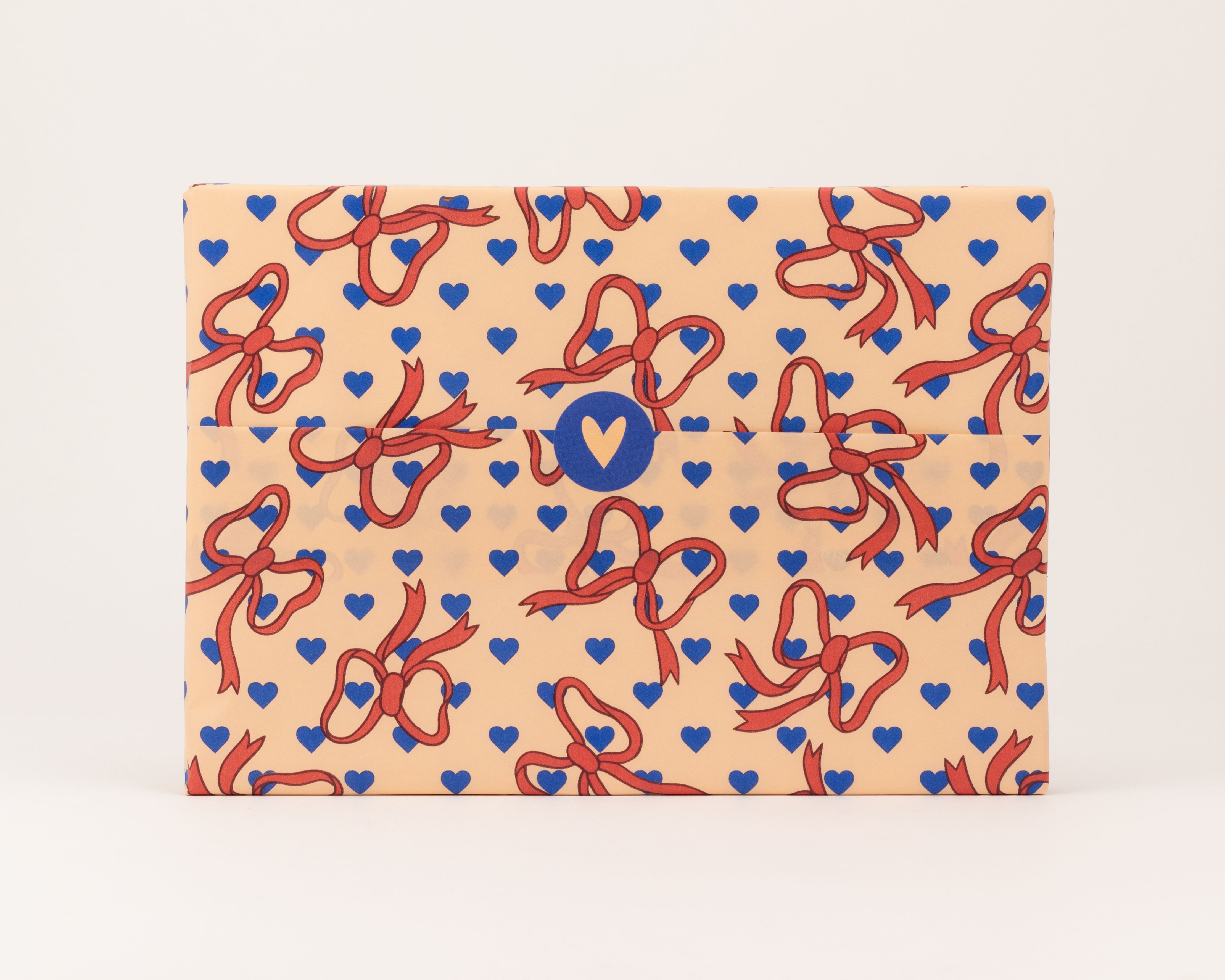 Seidenpapier mit einem Muster aus roten Schleifen und kornblumenblauen Herzen auf pfirsichfarbenem Grund