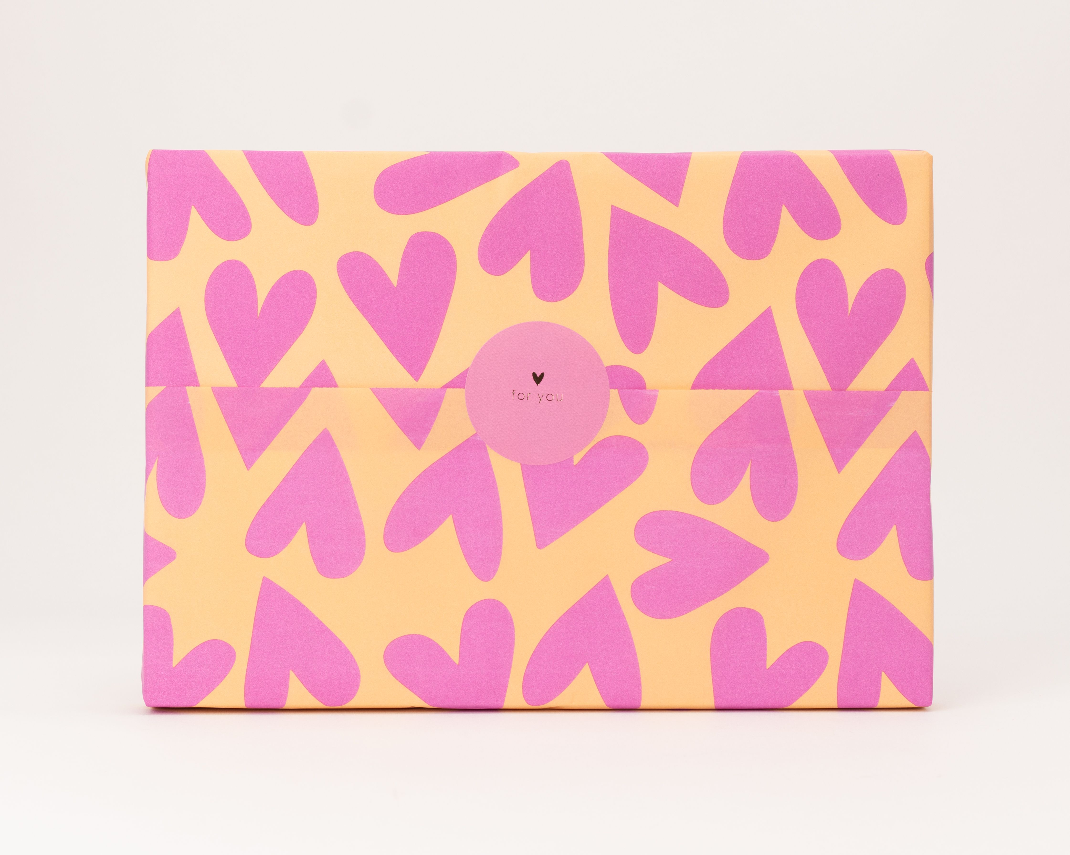 Seidenpapier mit pinken Herzchen auf orangefarbenem Grund. Darauf ein rosa runder Aufkleber mit for you Schriftzug