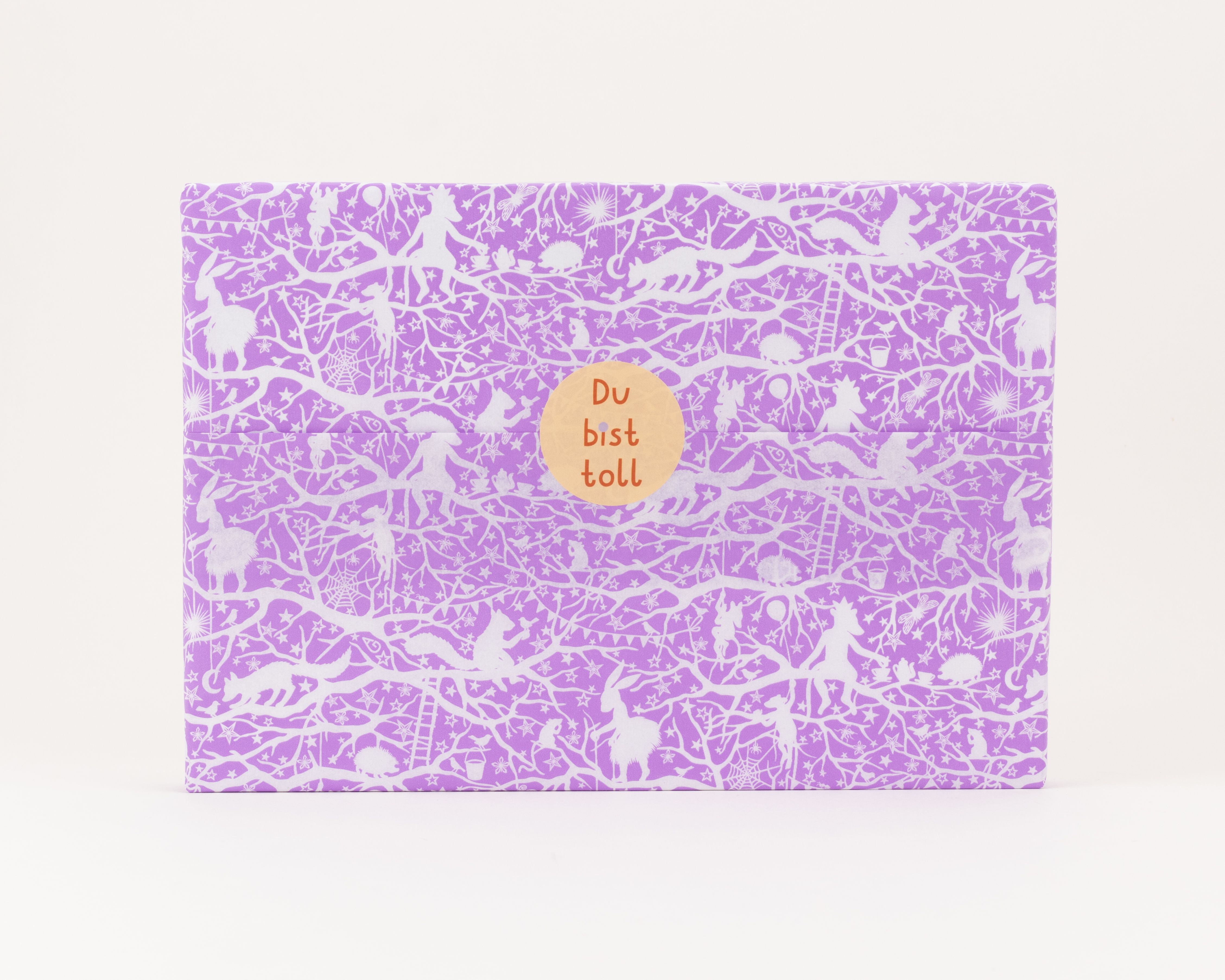 Seidenpapier in hellem Lila mit weißen Märchenwaldmotiven. Darauf ein runder, orangefarbener Aufkleber mit dem Text Du bist toll