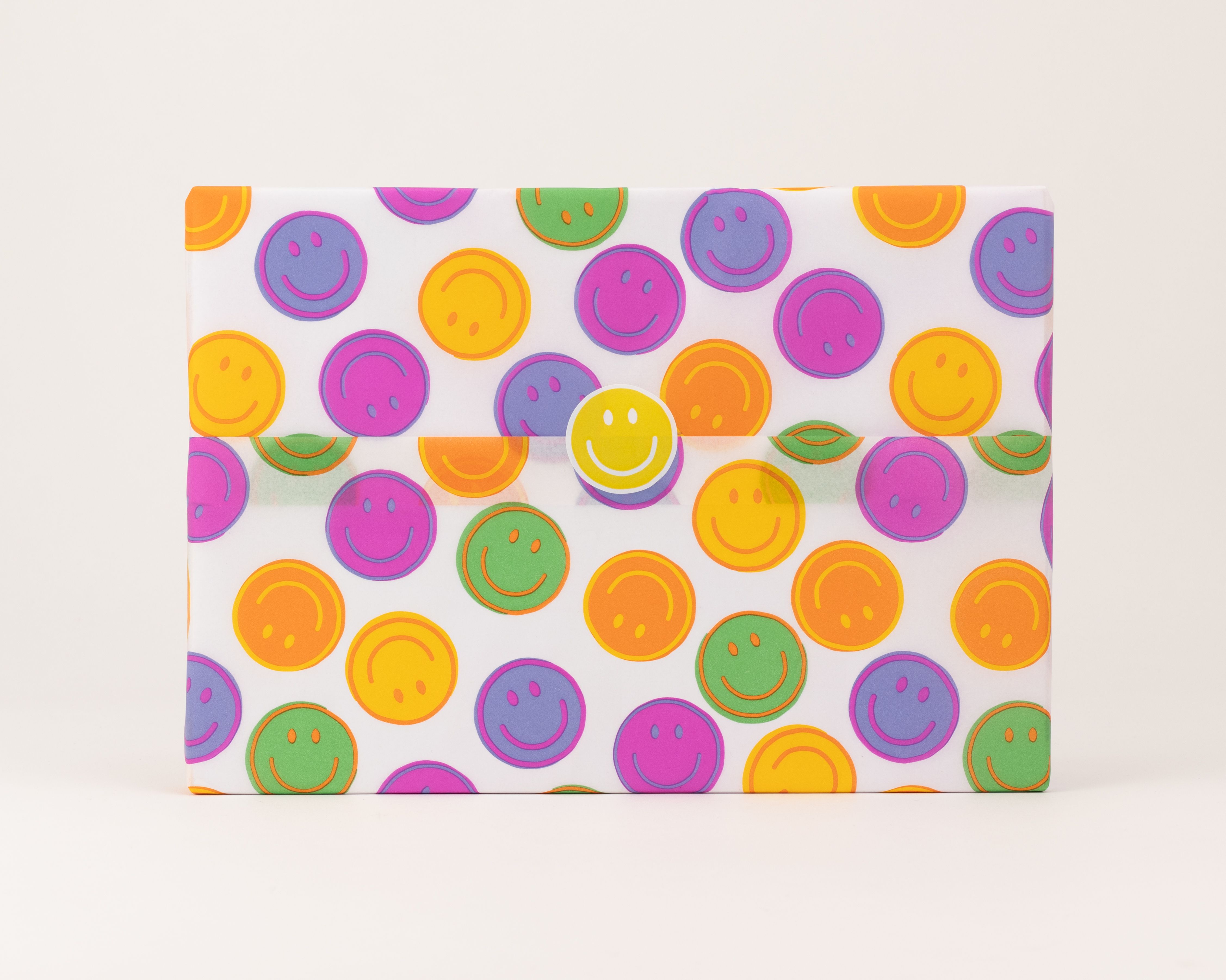Seidenpapier mit buntem Smiley-Muster in leuchtenden Farben auf weißem Grund. Ein runder, gelber Smiley-Aufkleber